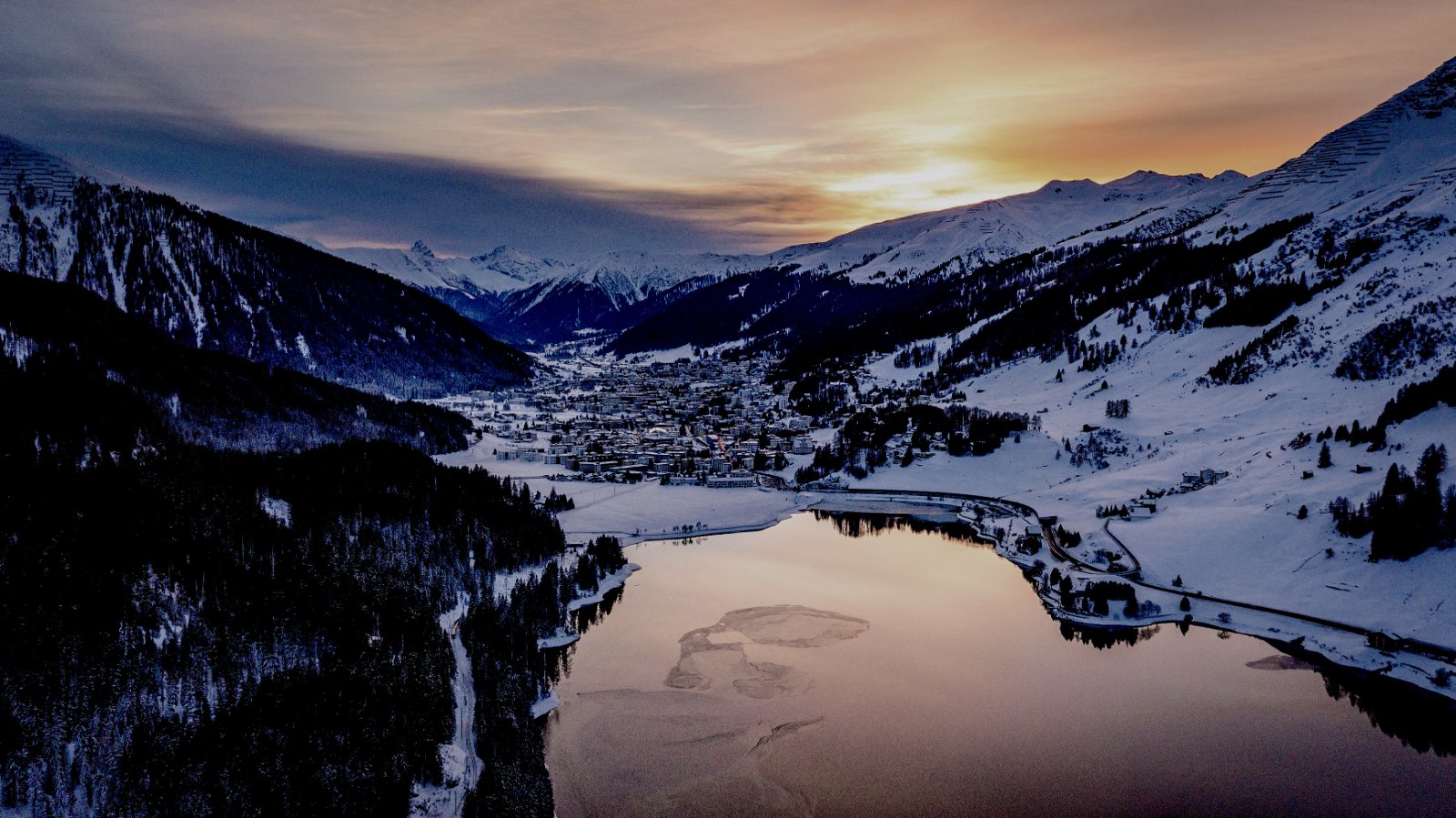 Black-and-white wide landscape of Davos and the Landwasser valley in deep winter, snow-covered peaks and the town lights