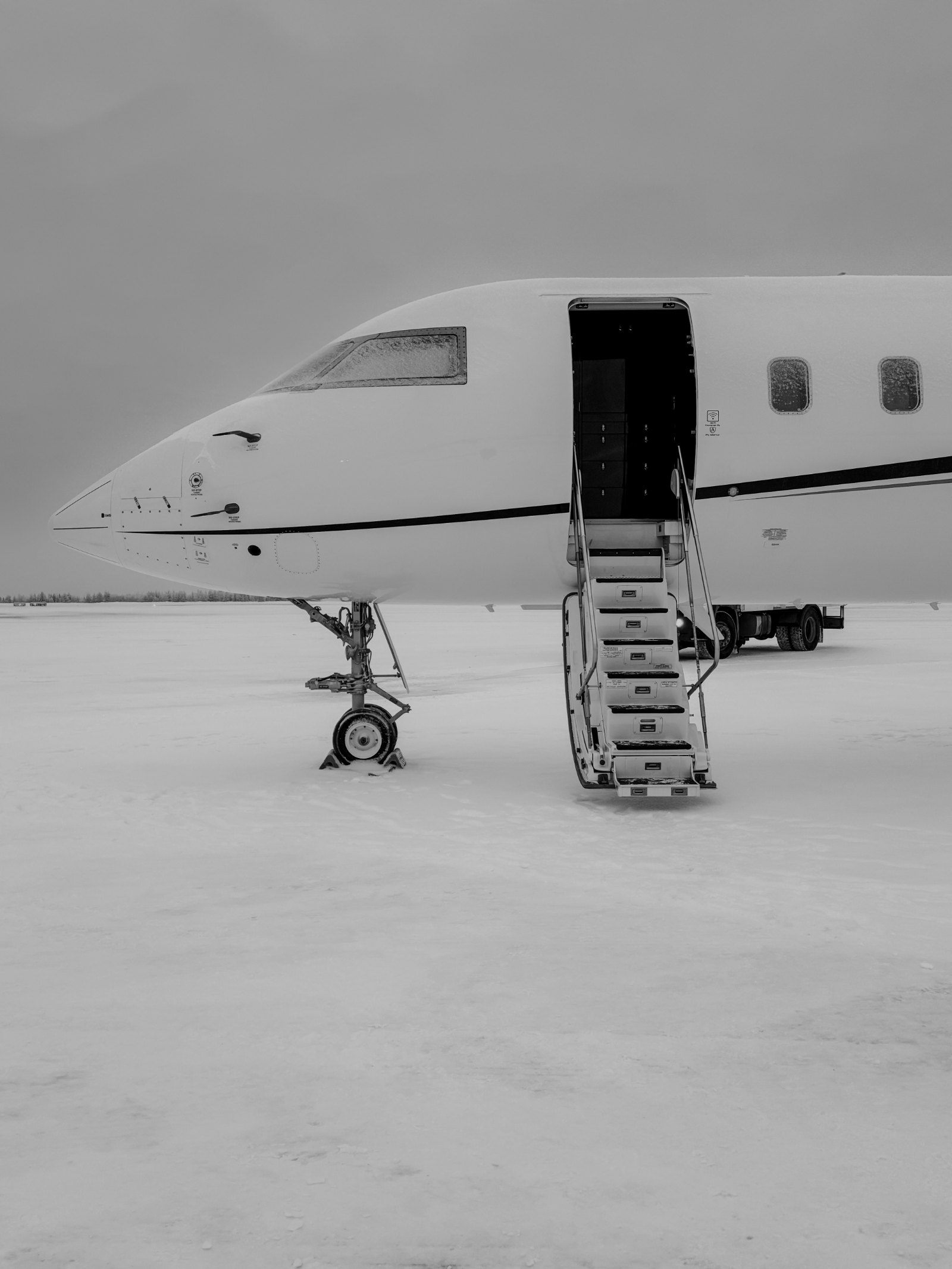 Black-and-white image of a busy private aviation apron in winter with several business jets parked nose to tail, ground