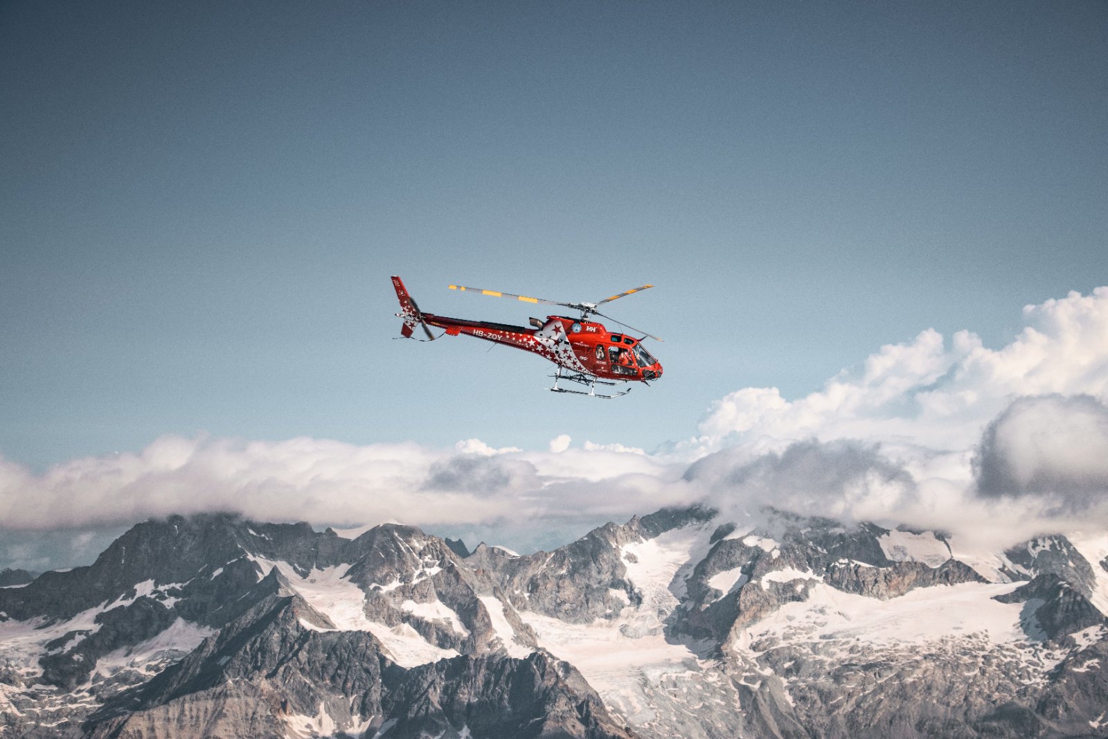 Black-and-white photograph of a helicopter lifting off from a snowy mountain helipad, or a car on a winding Alpine road