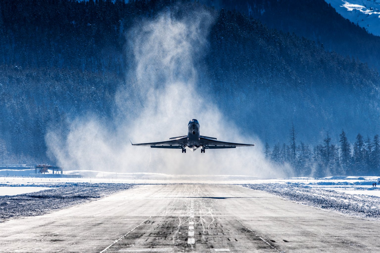 Black-and-white photograph of a business jet on a snow-edged apron at an Alpine airfield such as Samedan, mountains risi