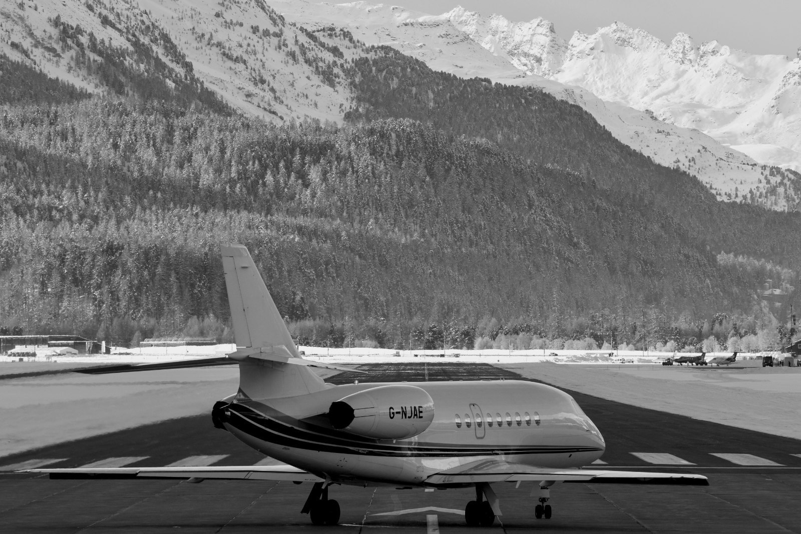 Understated black-and-white photograph of a helicopter on a snowy alpine pad or a private jet on the apron at Engadin Ai