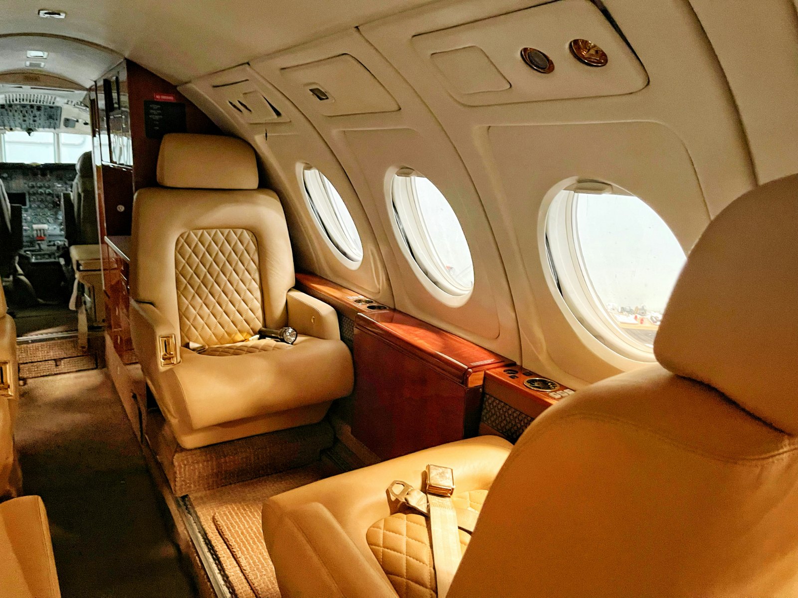 Business jet cabin with a cream quilted leather seat, round windows and the cockpit beyond