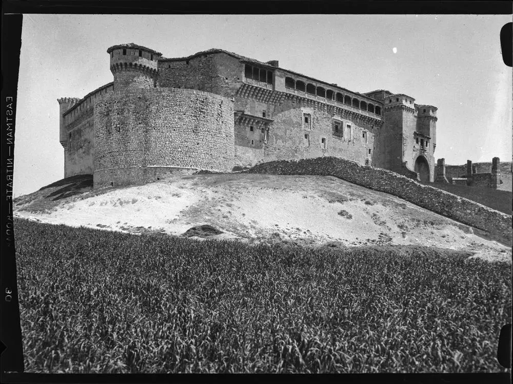 Castillo de Cuéllar [Vista lateral con dos torres circulares en las esquinas y muro de piedra que separa los campos de cultivo de la explanada delantera].