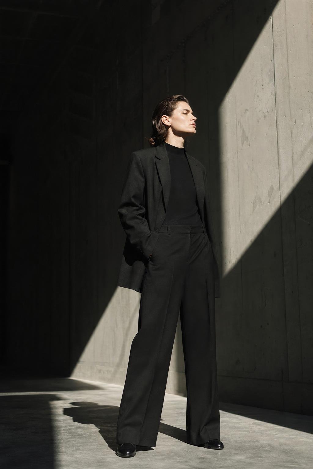 A confident figure standing in hard directional light inside a concrete studio