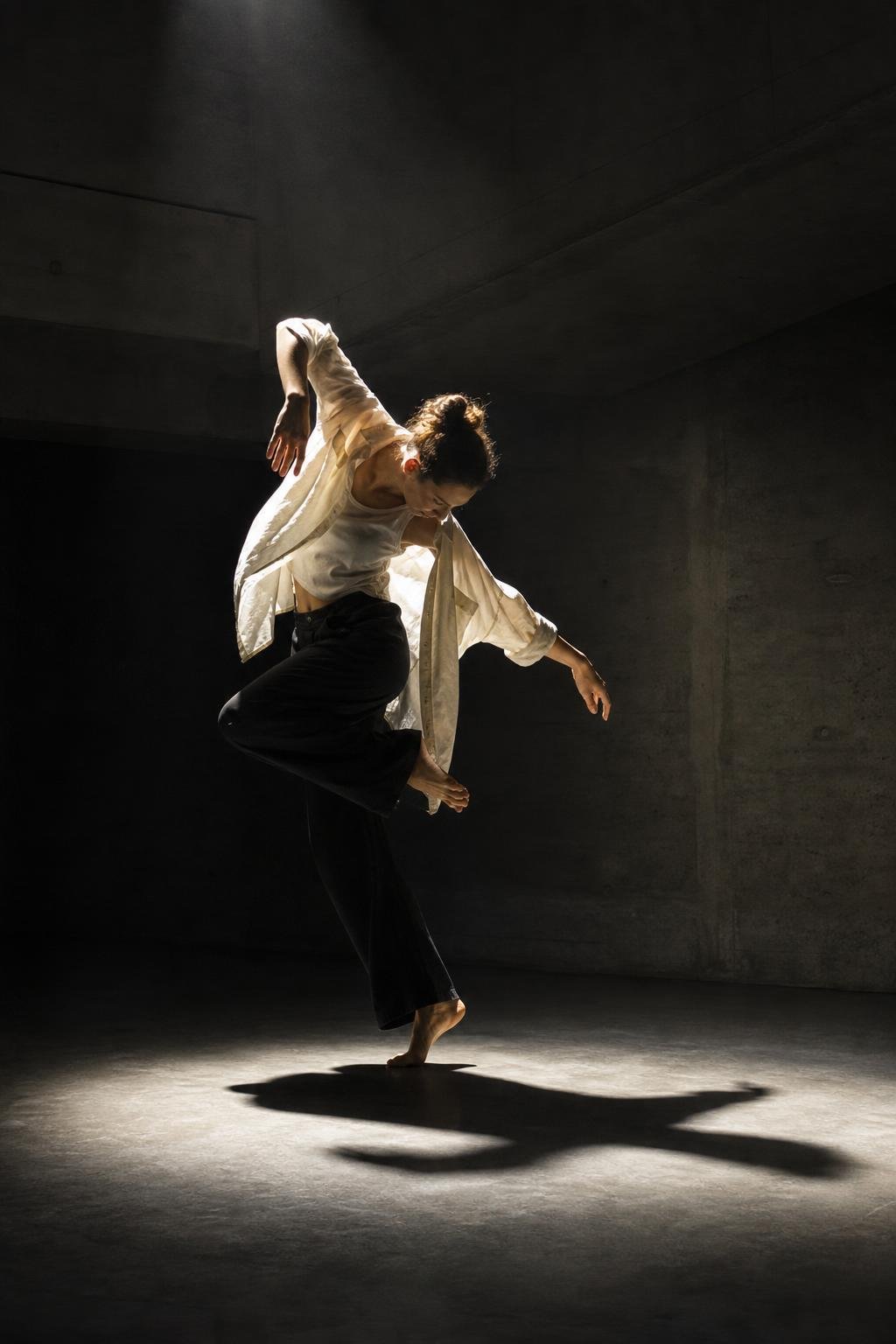 A dancer mid-motion under a hard spotlight in an empty concrete studio