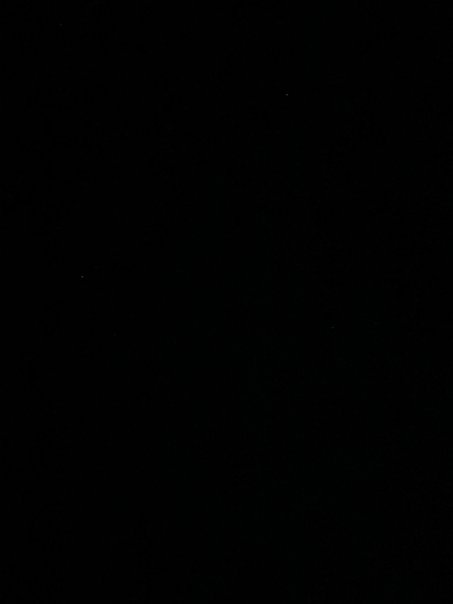 The image is a black frame with a few white and blue specks, suggestive of stars or distant lights. There is no identifiable city, location, people, subjects, objects, or actions visible in the frame. It is not possible to determine the location in the city of Cetinje, Montenegro.