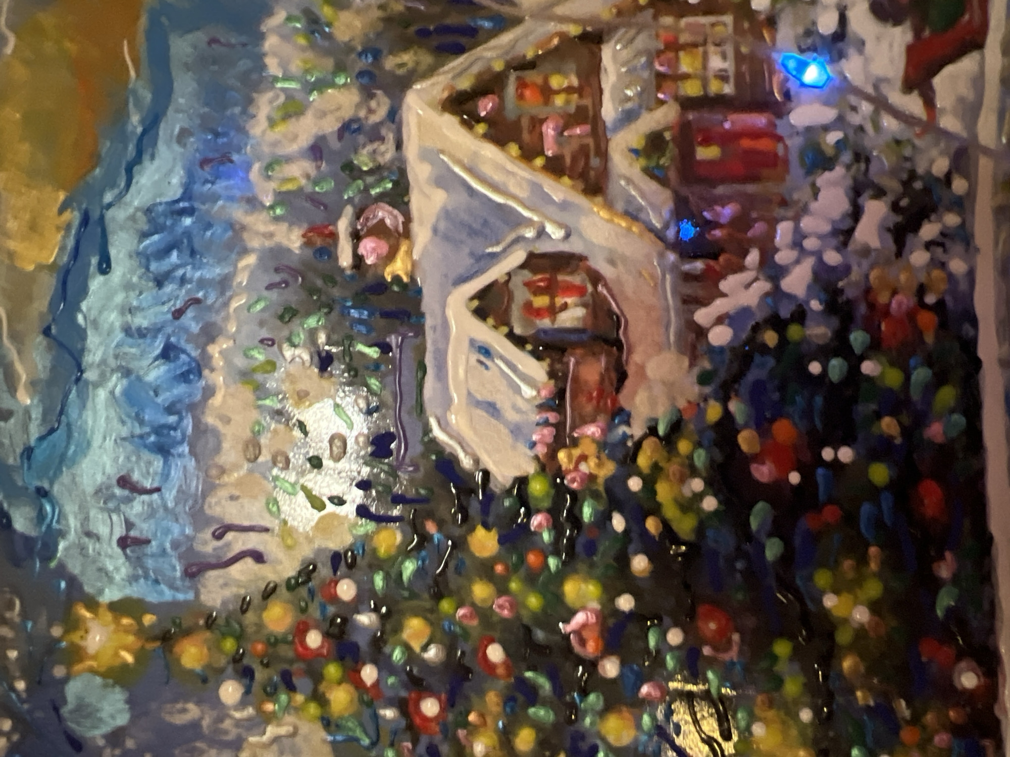 This is a close-up, textured painting of a festive winter scene. A decorated Christmas tree, adorned with colorful baubles, stands to the left of a snow-covered house. The house features illuminated windows and a chimney with smoke. The background consists of abstract blue and yellow brushstrokes suggesting a night sky or festive lights. There are no visible people or specific landmarks indicating a location in Minsk, Belarus.