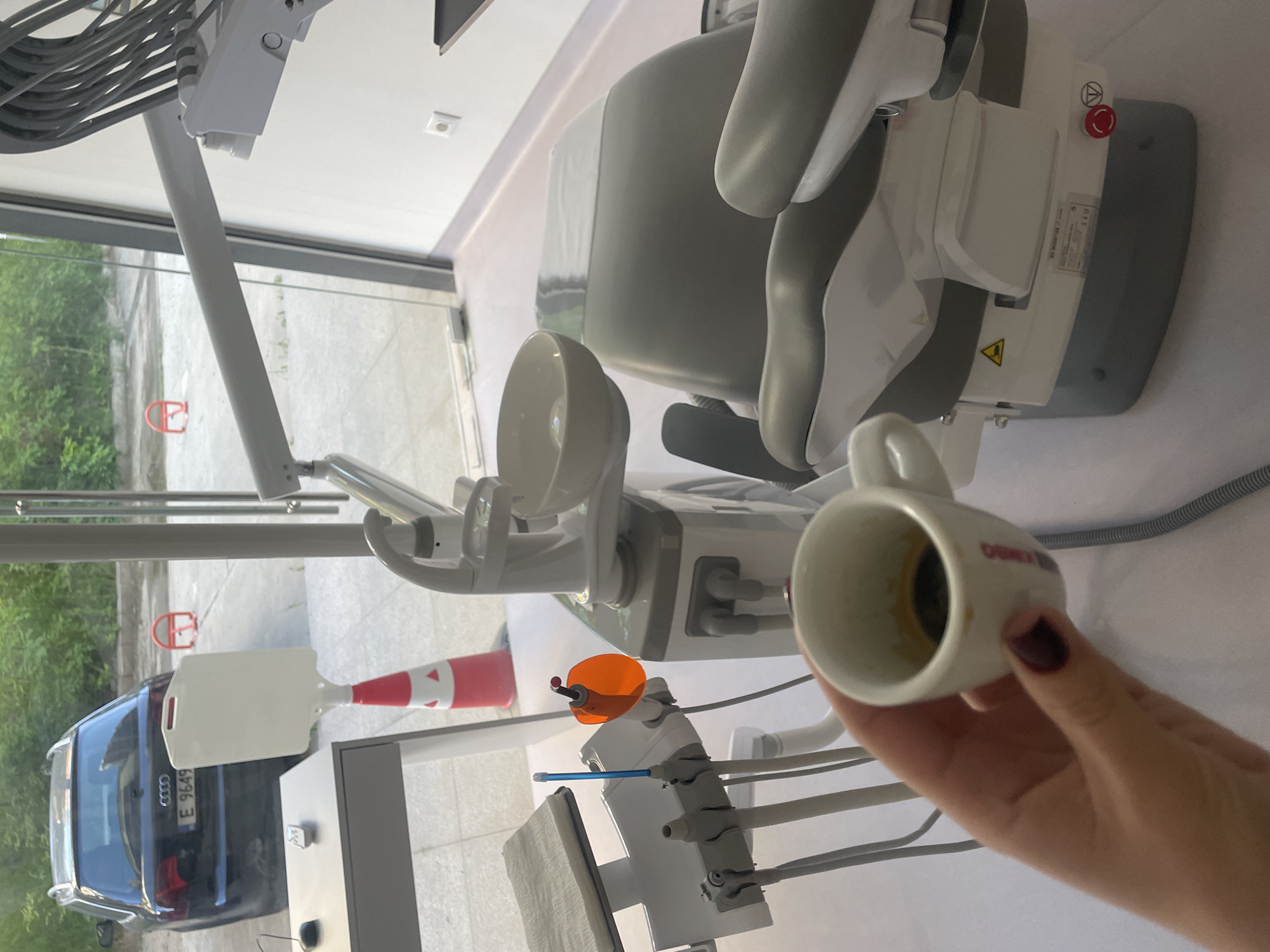 A dentist chair is situated in a room in Sofia, Bulgaria, near a window where a dark blue Audi with license plate E 9649 BK is seen. A hand holds a coffee cup with coffee grounds at the bottom.