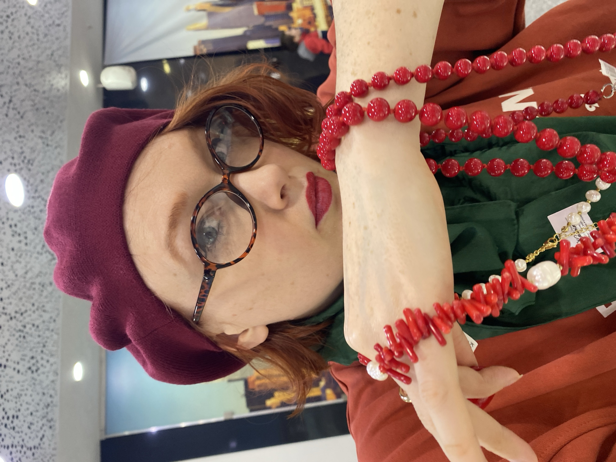 A portrait of a woman with red hair and freckles, wearing a burgundy beret and tortoiseshell glasses, is presented. She is also adorned with multiple strands of red beaded necklaces and bracelets. Her lips are painted with a matching shade of red lipstick.
Due to the limited visible details, it is impossible to confirm the location is Yekaterinburg, Russia, or to definitively identify specific actions or interactions. However, the image suggests she may be posing for a portrait.