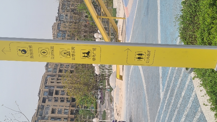 The image shows a yellow signpost in a park located at the coordinates (latitude: 29.333, longitude: 106.254) in Chongqing, China. The signpost is in front of a residential building and is surrounded by greenery. The signpost has several directions to different locations in the park, including a bubble world, a cloud amusement park, a dance floor, and public restrooms. The signpost is also near a yellow slide. The image was likely taken from a low angle, focusing on the signpost. There are no visible people in the image.