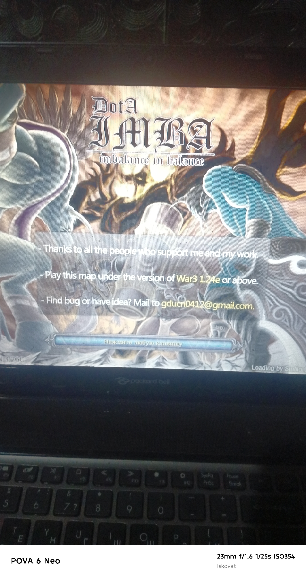 A laptop screen displays the title screen of a game called "DotA IMBA" with the tagline "imbalance in balance." Below the title, there are lines of text: "Thanks to all the people who support me and my work," "Play this map under the version of War3 1.24e or above," and "Find bug or have idea? Mail to gducn0412@gmail.com." At the bottom center of the screen, there is text in Russian that translates to "Press any key." The laptop's keyboard is visible at the bottom of the image. The image is dated with technical specifications: "23mm f/1.6 1/25s ISO354" and a photographer's name, "Iskovat." The location is specified as Pastki-Peshkurgan, Uzbekistan.