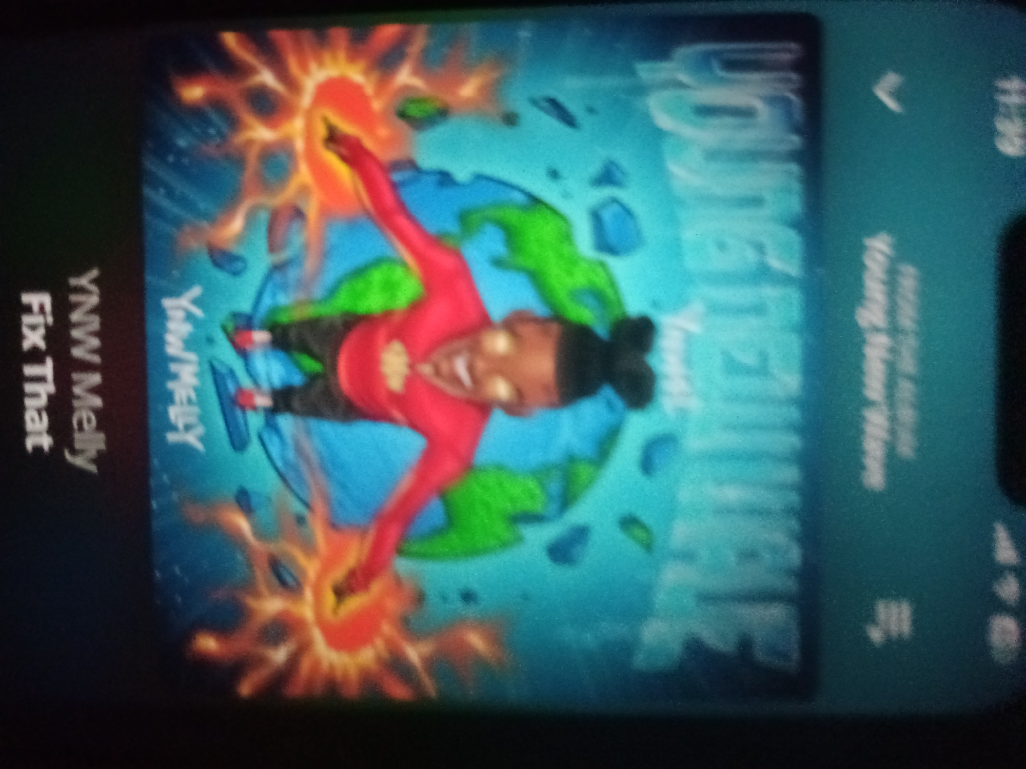 The image shows a smartphone screen displaying album art for the song "Fix That" by YNW Melly. The album art features a cartoonish character in a red outfit with fiery effects around them, set against a blue and green background resembling Earth. Text on the left side of the screen reads "YNW Melly Fix That". On the right side, larger text in a stylized font is partially visible, along with smaller text that appears to be "Young Never Knows". The phone screen is oriented vertically, and the image quality is poor, with a significant amount of grain and blur. There is no indication of the location being Jalingo, Nigeria, or any other specific city. The context suggests a person is viewing music playback on their device.