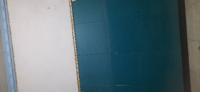 The image shows a wall in an indoor space. The wall is divided into two sections. The top section is painted white, and the bottom section is a darker blue. The wall has a small, decorative trim at the top. There is a slight discoloration in the lower portion of the blue wall, indicating a possible defect or damage. The image depicts the wall with nothing else in the frame. The location is not visible in the image, however the provided coordinates indicate it is located in Kecamatan Candi, Indonesia.