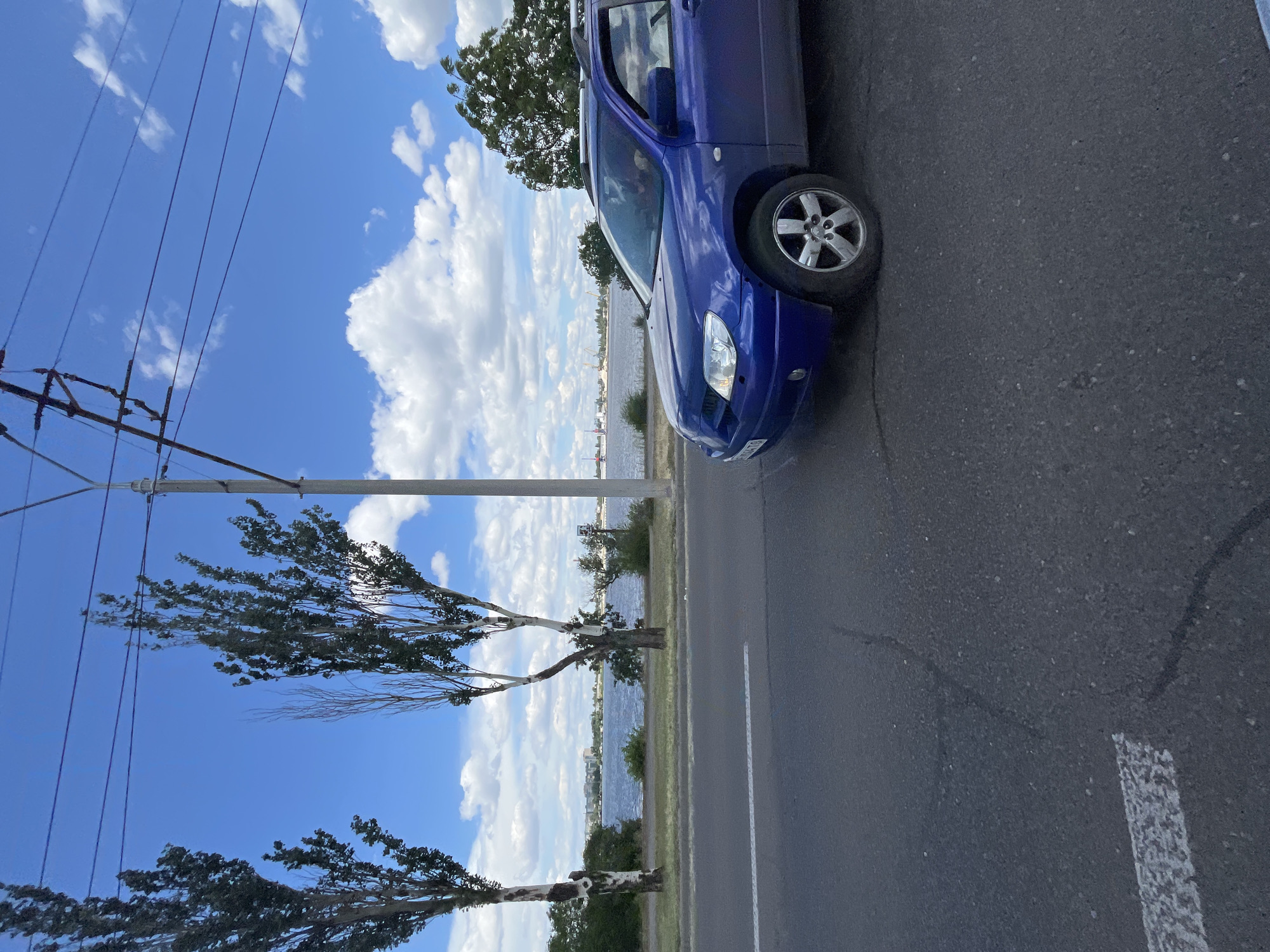 The image shows a blue car parked on the side of a road, with the sea in the background. The sky is blue with white clouds, and there are trees on the left side of the image. The image is taken from a low angle, looking up at the car and the sky.
The car is a hatchback, and it is parked on a paved road. The road has a white line painted on it, indicating a lane. The sea is visible in the background, and there are some buildings on the other side of the sea. The sky is blue with white clouds, and the sun is shining. There are trees on the left side of the image, and they are green and leafy. The image is taken in daylight, and the weather appears to be good.
The image is taken in a coastal area, and it is likely a sunny day. The car is parked on the side of the road, and it is not in use. The sea is calm, and there are some boats in the distance. The trees are green and leafy, and they are providing shade. The sky is blue with white clouds, and the sun is shining. The image is taken in daylight, and the weather appears to be good.
There is no visible text in the image. The image is of a car parked on the side of the road, with the sea in the background. The sky is blue with white clouds, and there are trees on the left side of the image. The image is taken from a low angle, looking up at the car and the sky.