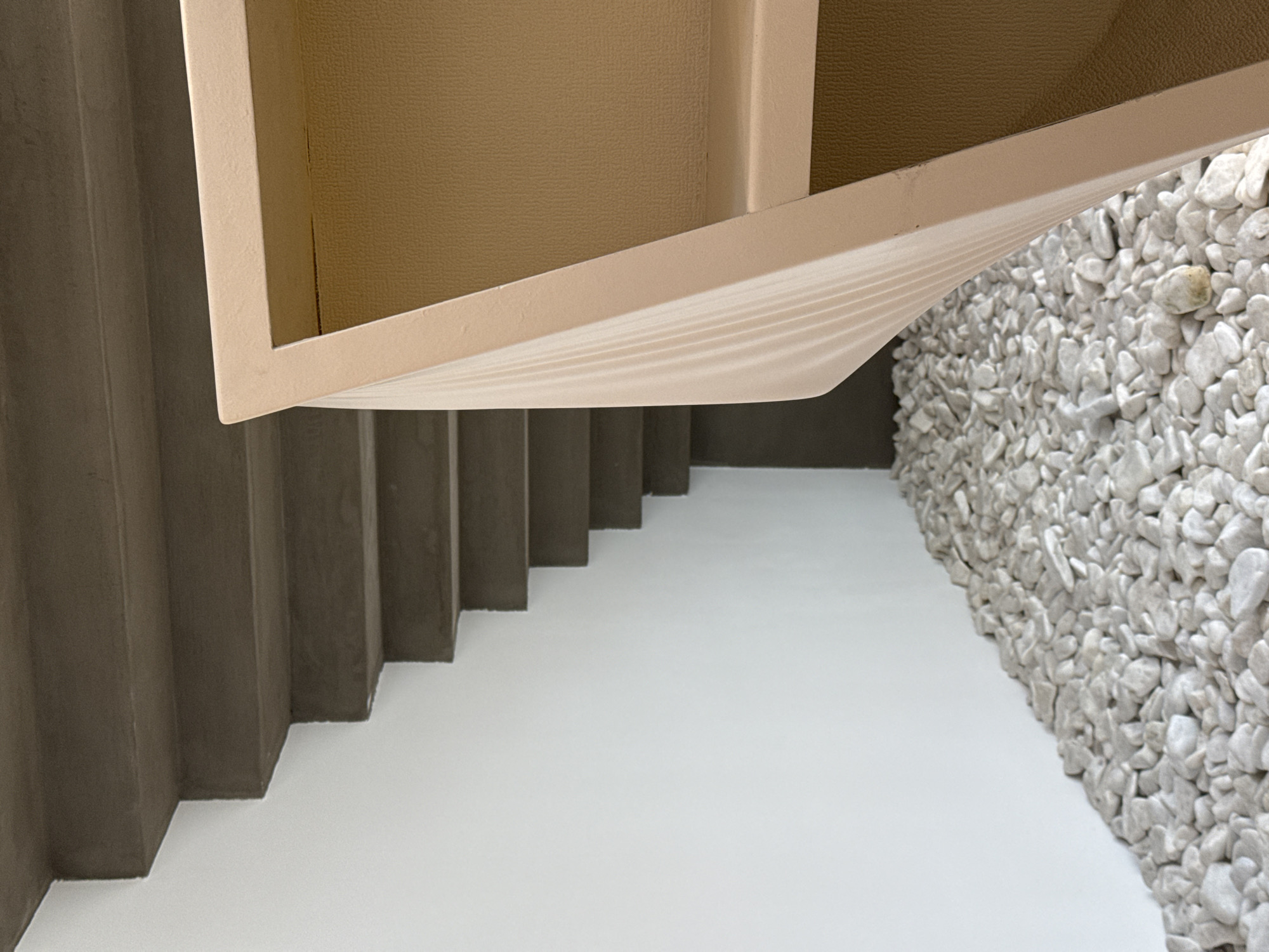 The image depicts a portion of an interior architectural space. There are stairs with a beige-colored wall lining the left side. The treads of the stairs are gray and the floor is white. Adjacent to the stairs is a wall entirely covered with small white stones. In the upper portion of the frame, there is an opening to a box, which is beige in color. There is no clear indication of the location being Moscow, Russia. No people or interactions are visible.