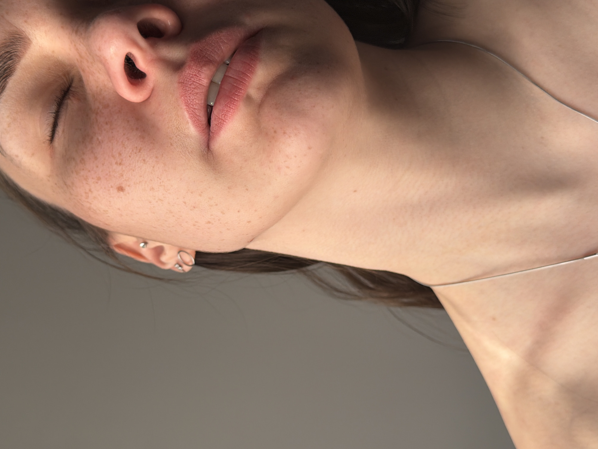 A close-up, vertically oriented image shows a person's face and neck against a gray background. The person's eyes are closed and freckles are visible on their face. They have a silver necklace. The location in the city of Chaikovsky, Russia is not determinable from the image.