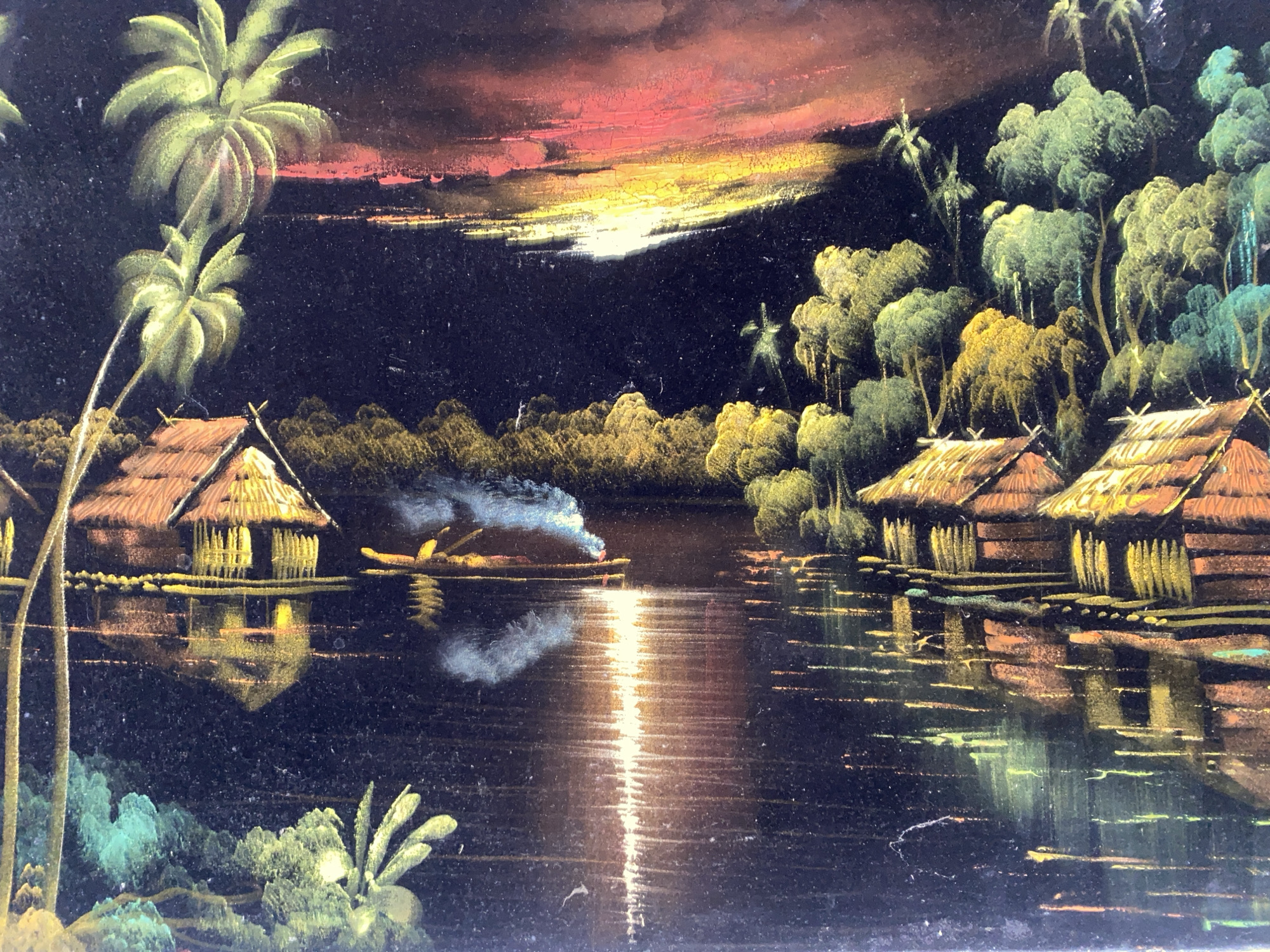 The image depicts a nighttime scene of houses on stilts lining a body of water, likely a river or lake. The houses have thatched roofs and are illuminated with a warm light, reflected in the water. A small boat with a figure is on the water, emitting smoke. Palm trees and other vegetation flank the houses. A vibrant sunset or sunrise is visible in the background, casting a colorful glow across the sky. The style of the image suggests it may be a painting or a print. The city location of Tinaquillo, Venezuela is not evident in the image itself.