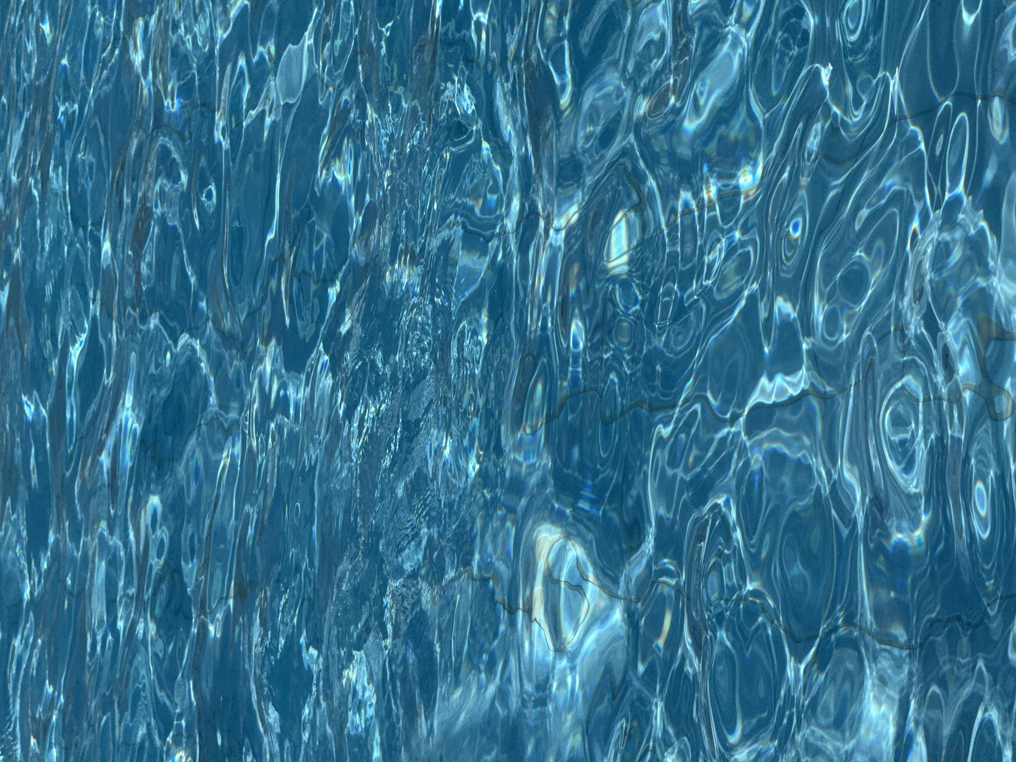 The image shows the surface of a swimming pool in Bat Yam, Israel. The water is a clear blue, and the sunlight creates patterns on the bottom of the pool. The tiles of the pool are visible through the water. No people or other objects are visible.