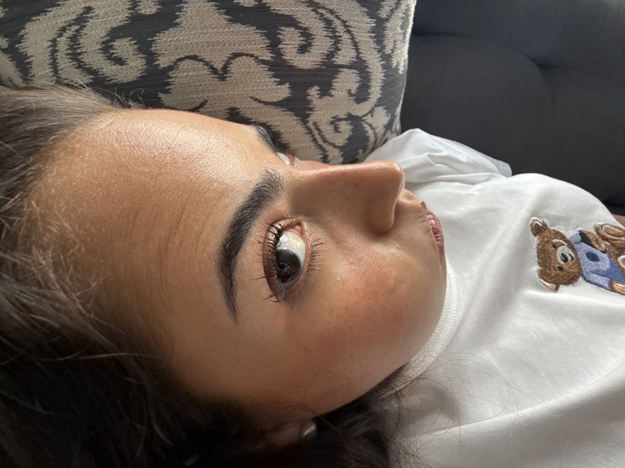 A close-up shot focuses on a person lying down. The person is fair-skinned with dark hair. A decorative pillow is behind the person. The person wears a white shirt. The setting is indoors. There is no indication that the scene is in San Bernardino Tlaxcalancingo, Mexico.