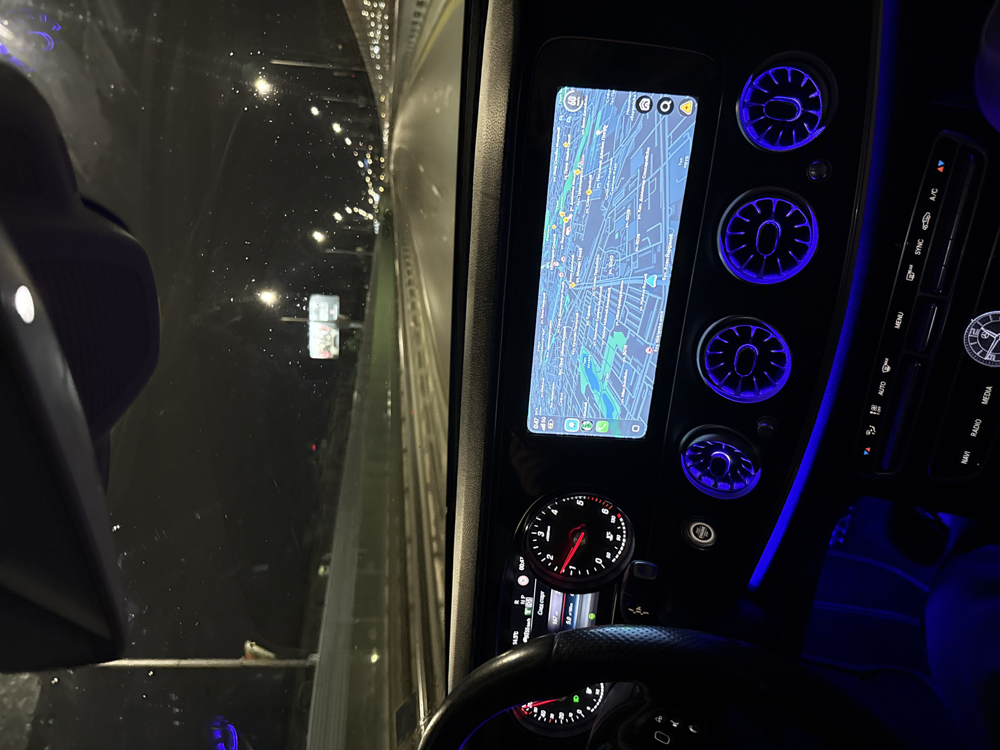 The image shows the interior of a car driving at night. A navigational system display is on in the center console, showing a map of Sofia, Bulgaria. Specific streets include ул. Посланик Джеймс Парове, YA. Kan. Au Списаревски, and бул. Асен Йорданов. The speedometer reads approximately 40 km/h. The dashboard displays a temperature of 14.5℃. Blue ambient lighting is visible within the car. Outside, it appears to be raining, and traffic lights are visible.