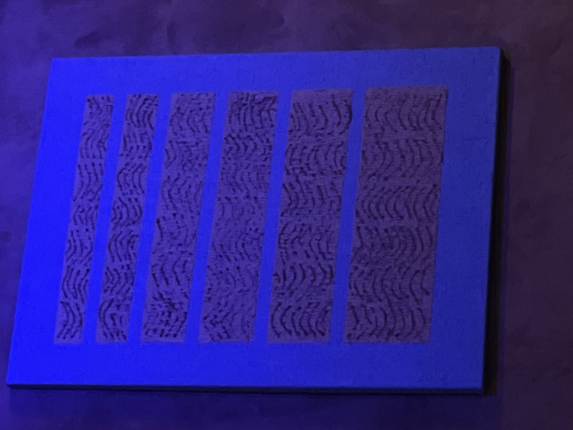 An abstract painting with a bright blue background features six horizontal rectangular sections filled with a textured, dark purple pattern. The pattern in each section consists of repeating, wavy, parallel lines that create a somewhat organic or naturalistic appearance, possibly mimicking wood grain or ripples. The painting is displayed on a wall, which appears to be a dark, textured surface. The overall lighting suggests a dimly lit environment, possibly with a blueish hue casting onto the scene. The painting's location in Mũi Né, Vietnam is not evident from the visual information provided.