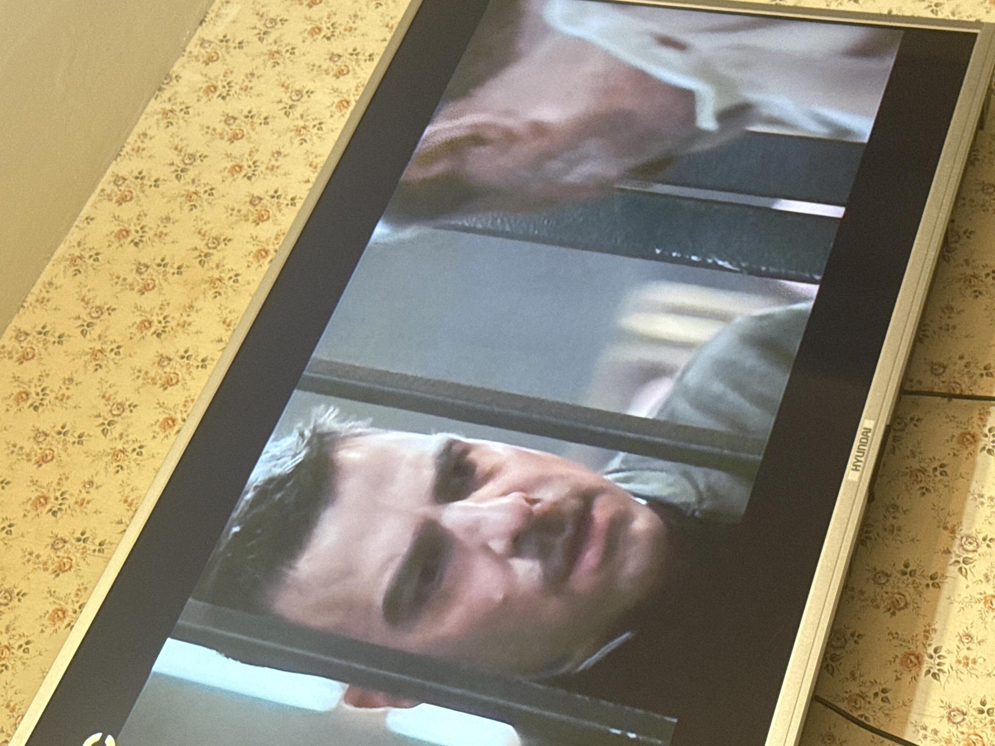 The image shows a close-up of a television screen with a man's face visible behind bars. The screen has the "HYUNDAI" brand name visible. The background includes a wall with a floral pattern. The image was likely taken indoors. There is no indication of the location being in Pushkino, Russia.