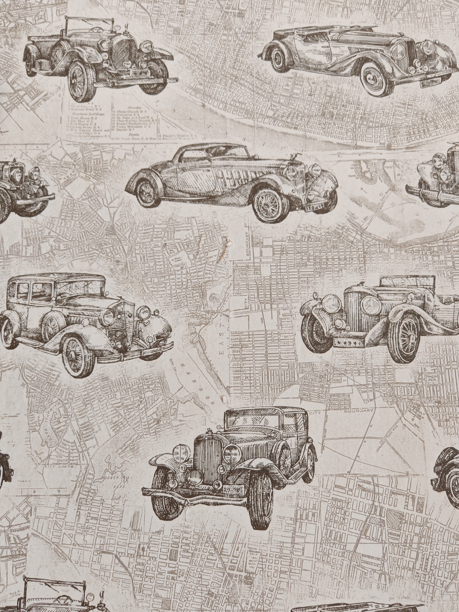 The image is a collage of vintage car illustrations superimposed on a sepia-toned map. The cars are depicted in a sketchy, artistic style, with varying models and types. Some are convertibles, while others are sedans. The map appears to be a detailed street grid, with street names and building outlines visible. The overall aesthetic is retro and somewhat aged, suggesting a historical or nostalgic theme. There are no people visible in the image. The city of Kumertau, Russia is not depicted or referenced in this image.