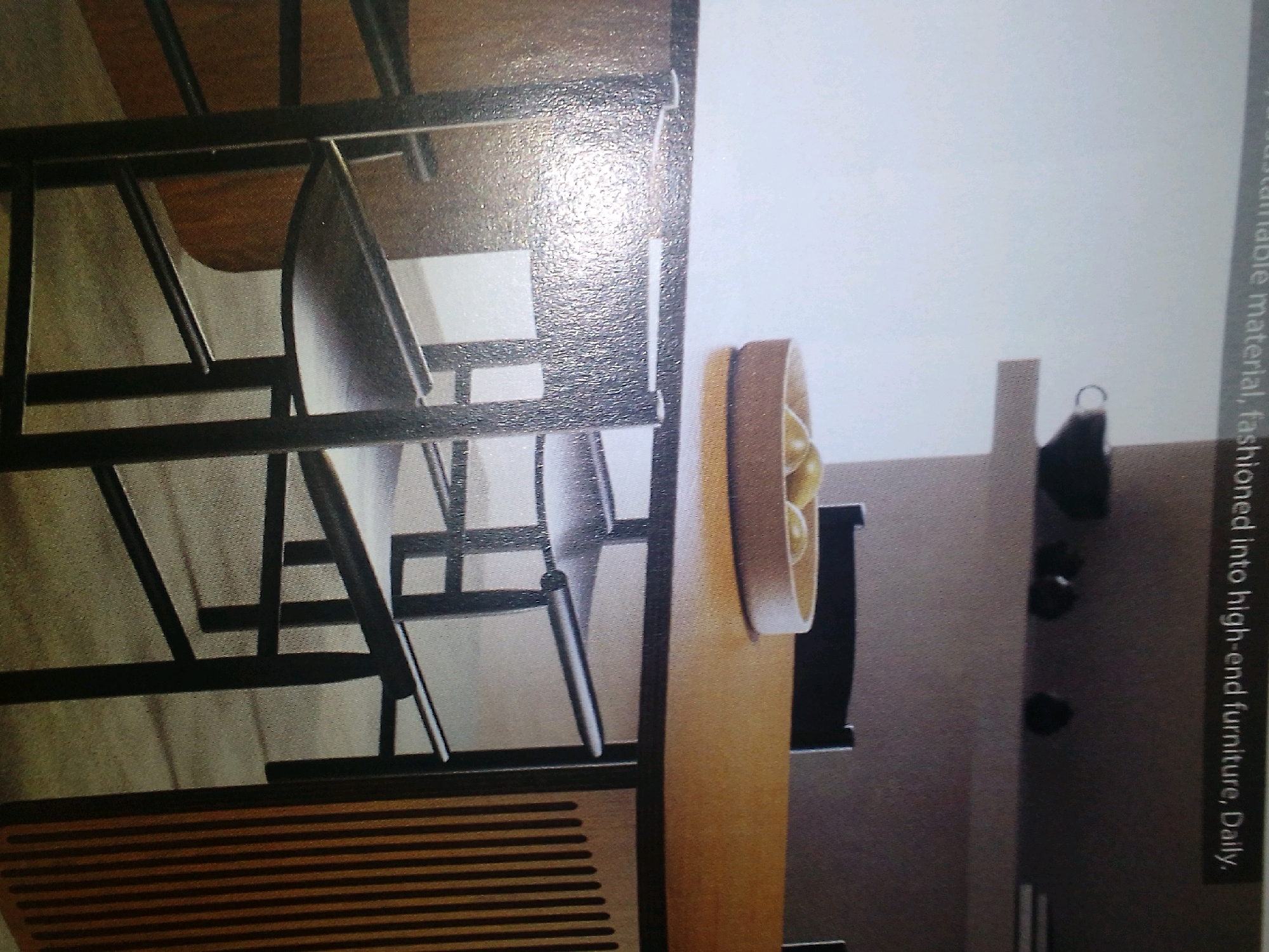 The image shows a close-up view of a contemporary furniture piece, possibly a shelving unit or display cabinet, made of dark metal and wood. The design features clean lines and geometric shapes. The left side of the frame reveals a structured arrangement of shelves and supports, with one shelf appearing to be made of a dark, glossy material and another of a lighter wood. Below this, there is a horizontal slatted section.
To the right, a tall, curved wooden element is visible, possibly part of the same furniture piece or an adjacent item. This element has a smooth, polished finish. Further to the right, a dark, amorphous shape is present, and a lighter vertical rectangular element is visible behind it. There is also a thin, dark object with a curved handle visible in the upper right portion of this section.
Text is visible along the far right edge of the image, oriented vertically. It appears to be a caption or descriptive text related to the furniture. The text reads "ioned into high-end furniture, Daily." The initial part of the text is obscured.
The image does not contain any information about the city of Winterveld, South Africa, nor does it depict any people, actions, or interactions. The scene is purely an interior shot focusing on the design and materials of the furniture.