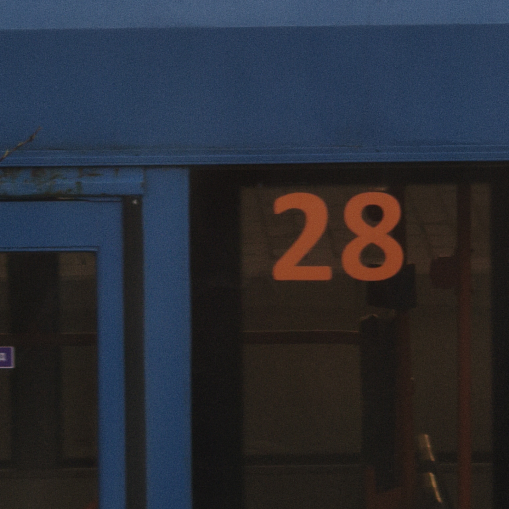 The image shows a blue building with the number 28 prominently displayed in orange on the window. The number appears to be illuminated. The door frame is blue. The location in the city of Hrodna, Belarus is unspecified.