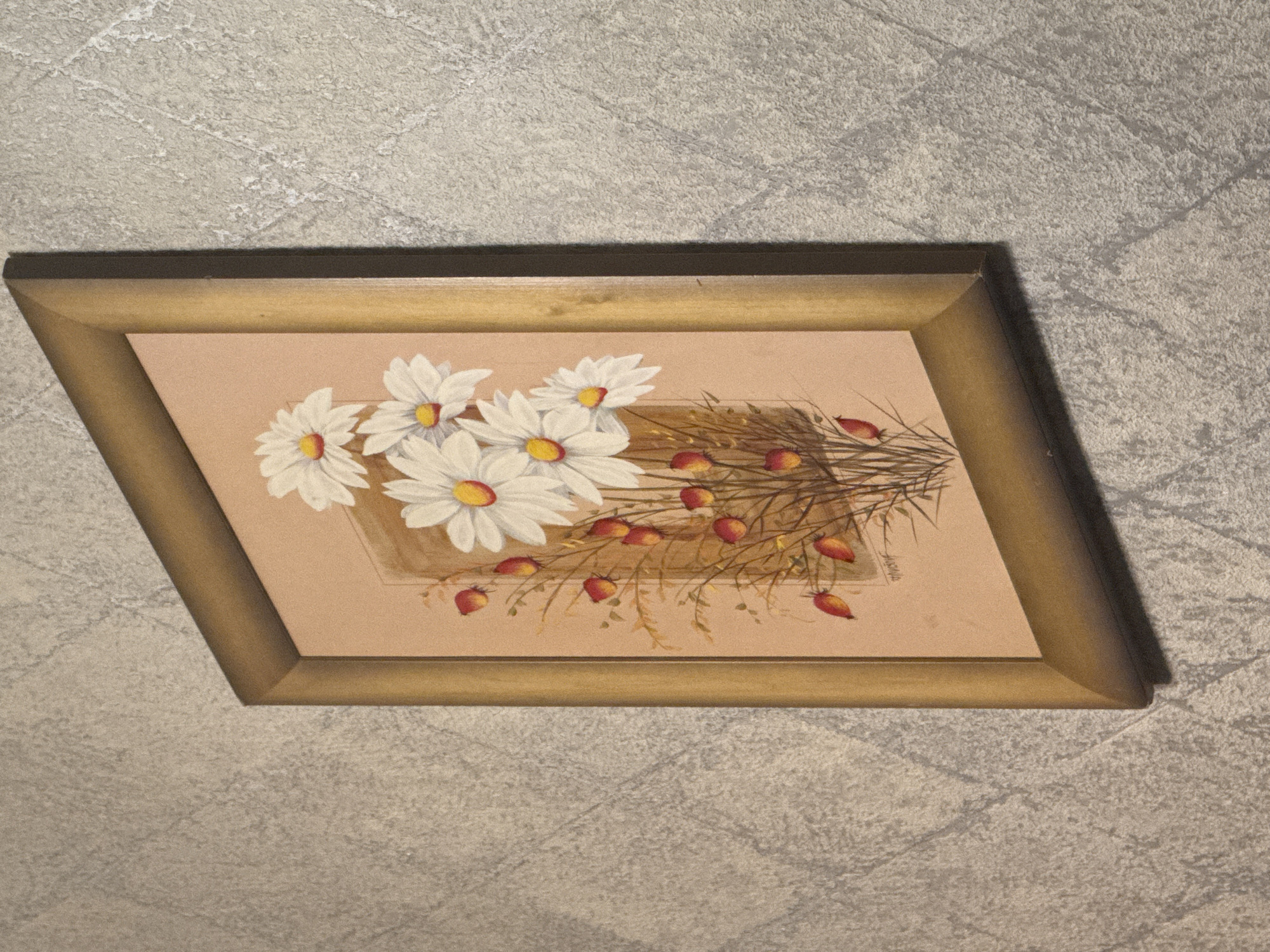 An oil painting of daisies and red berries in a gold frame hangs on a textured grey wall. The painting depicts a bouquet of white daisies with yellow centers, interspersed with stems bearing small, red, berry-like shapes. The background of the painting is a light peachy-tan color. The frame is a simple, beveled gold material. The wall behind the painting has a rough, uneven texture with a subtle diamond pattern. The lighting creates shadows on the wall, indicating the painting is illuminated from the side and above. There are no people or animals visible in the image. The location is not discernible from the image itself, and therefore, its connection to Kholmsk, Russia, cannot be confirmed.