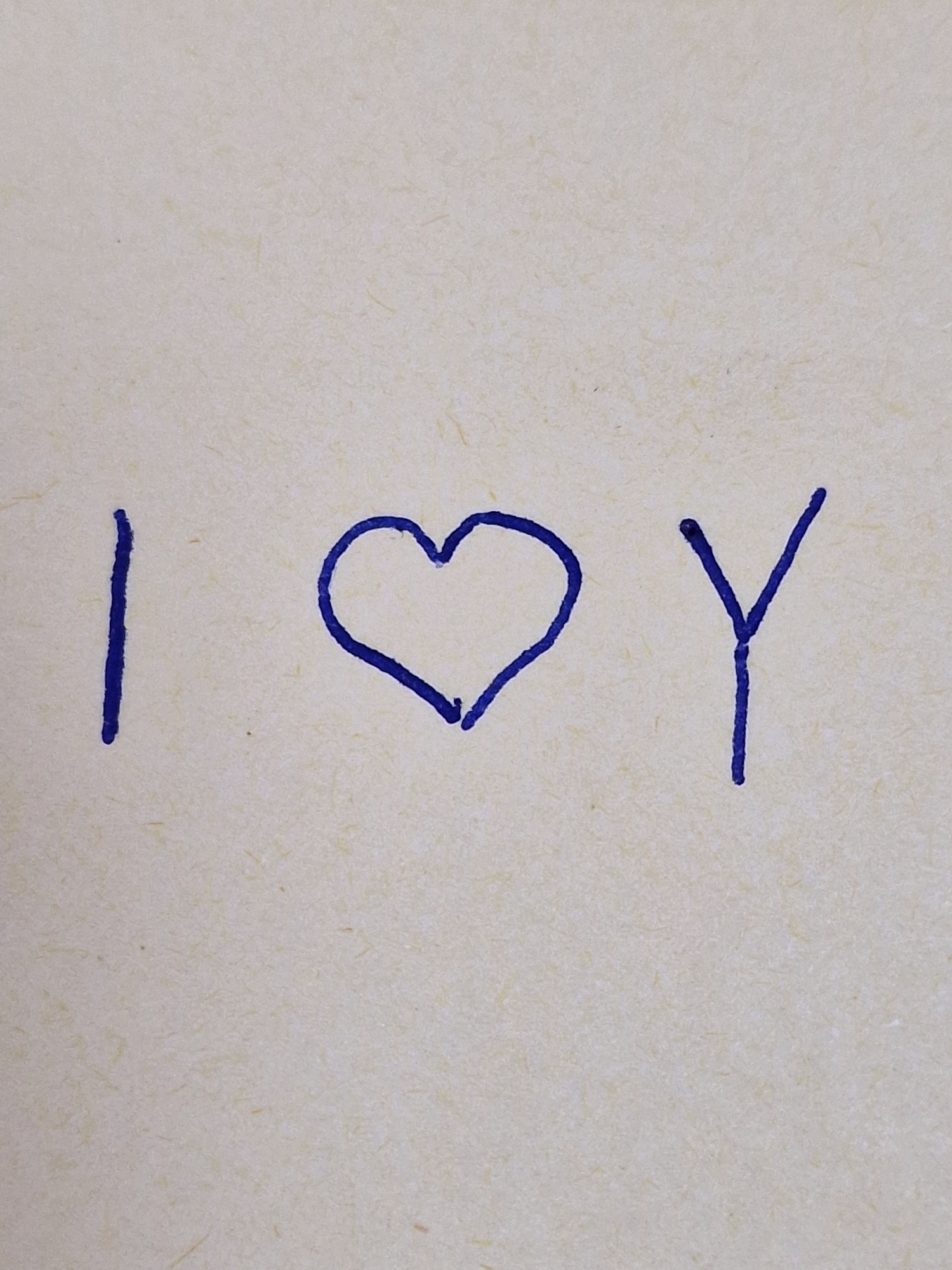 The image displays a handwritten message on a textured, light-colored surface, possibly paper. The message is written in blue ink and reads "I LOVE Y". The message consists of three elements: the letter "I", a heart symbol, and the letter "Y". The "I" is a vertical stroke. The heart is drawn with a rounded top and a pointed bottom. The "Y" is formed by two diagonal strokes meeting at a point. The writing is centered horizontally on the surface. The background is a light, speckled texture.