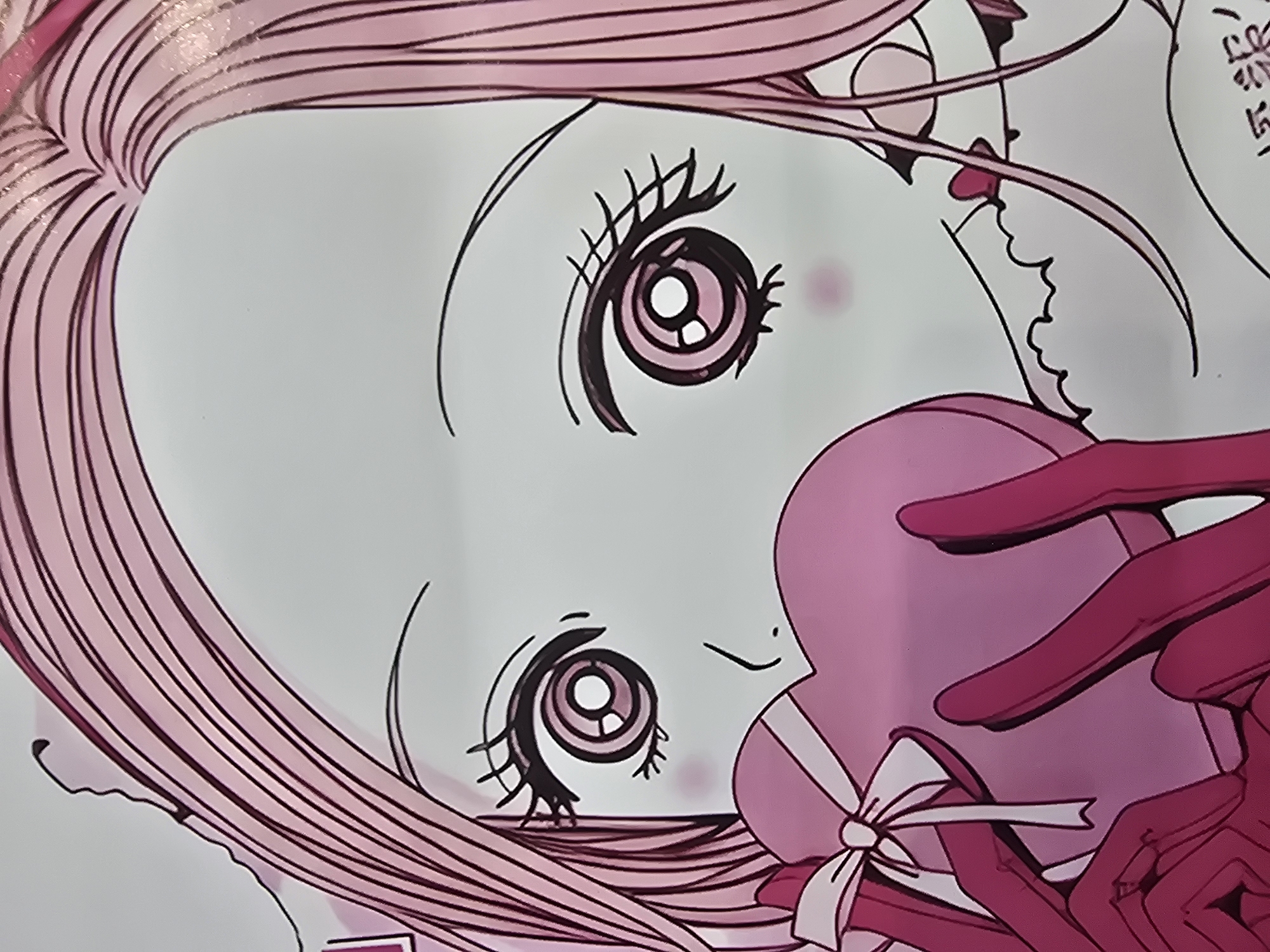The image is a close-up of an anime-style drawing of a young woman with long, pink hair and large, expressive eyes. She is holding a pink heart-shaped box tied with a white ribbon. Her hands, also pink, are visible as she holds the box to her face. She is wearing what appears to be a pink outfit with ruffled details around the neckline. The background is plain white, with some subtle pink blush marks on her cheeks. The drawing has bold black outlines and flat pink coloring, with some darker pink shading. There are no visible signs of the city of Ulan-Ude, Russia in this image.