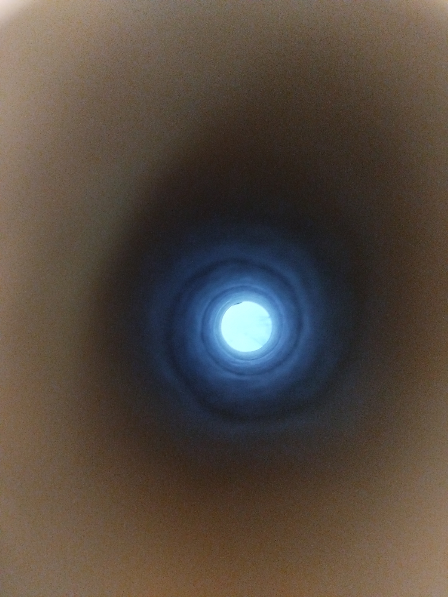 The image shows a close-up, overhead view looking down into a cylindrical object, possibly a pipe or tunnel. The interior walls of the cylinder appear to be dark and textured, with concentric rings creating a sense of depth. At the end of the cylinder, a bright, circular light source is visible, casting a bluish glow. The outer edges of the image are blurred and desaturated, suggesting a shallow depth of field or a dark environment surrounding the cylinder. There is no visible indication of people, specific objects, or actions. The setting of Kremenchuk, Ukraine, is not discernible from the visual information presented in the image.