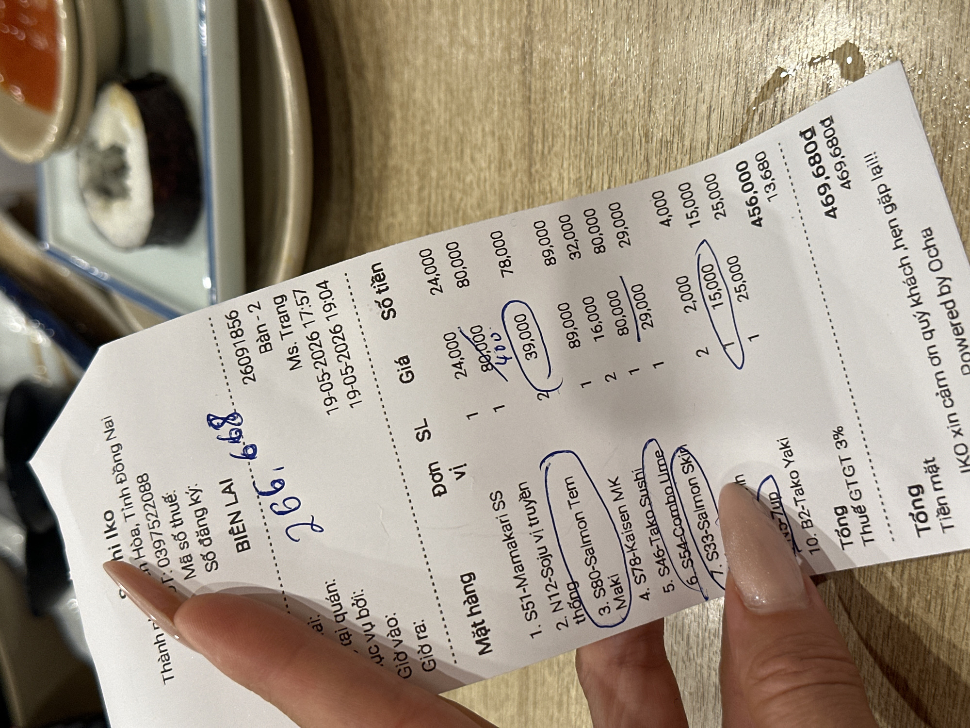 The image shows a receipt from "Iko," a restaurant in Đồng Nai, Vietnam. The receipt, dated May 19, 2026, lists several sushi and other Japanese dishes, including Mamakari SS, Soju, Salmon Tem Maki, Kaisen MK, Tako Sushi, Combo Ume, and Salmon Skin. The total bill is 469,680₫, including a 3% GTGT tax. A hand with manicured nails holds the receipt, with several items circled.
