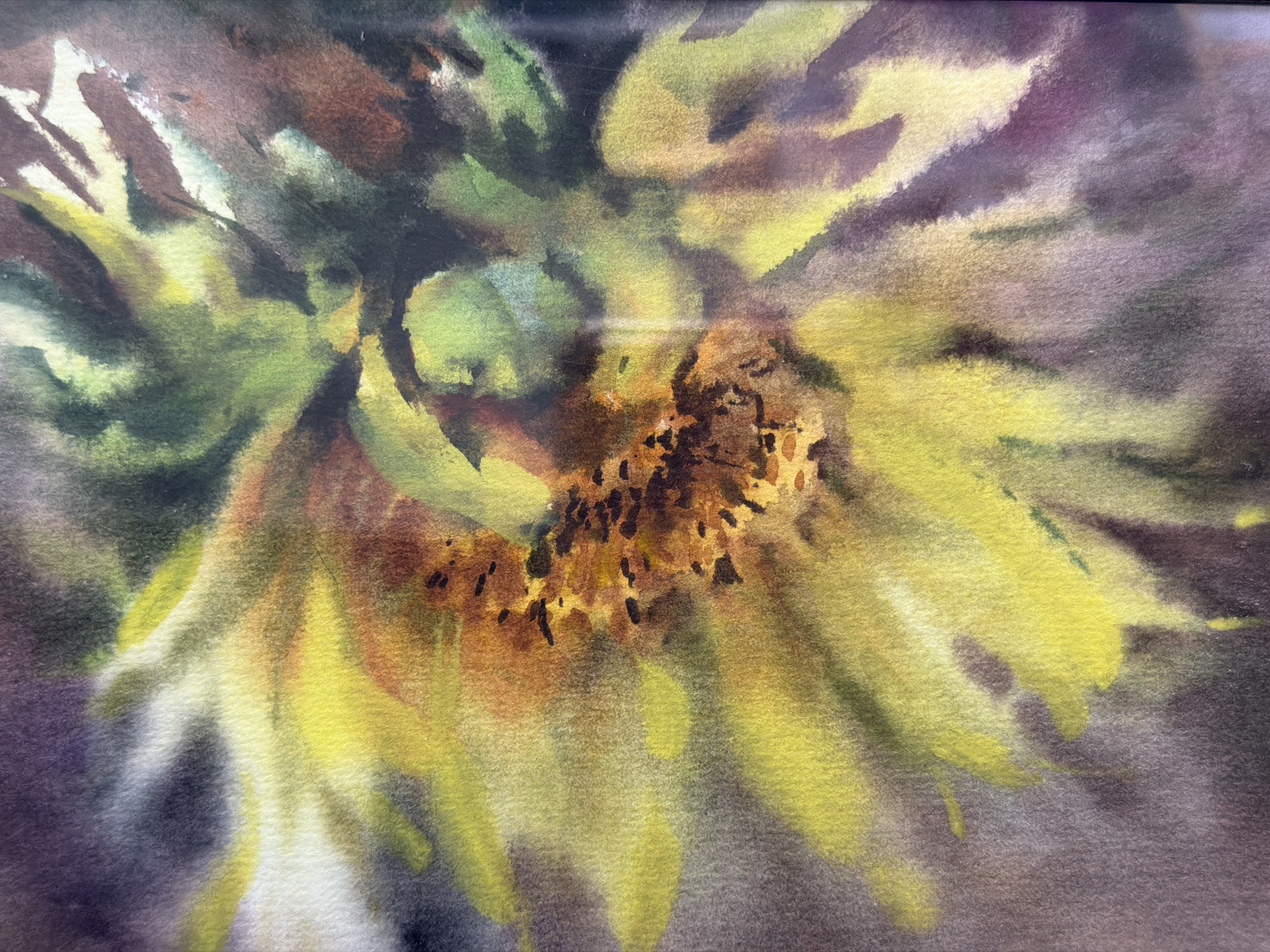 The image is a close-up watercolor painting of a sunflower. The center of the flower is depicted with dark brown and orange hues, with small black dots representing seeds. The petals are rendered in bright yellow and green, with some strokes of white and purple in the background, suggesting a diffused light source and a slightly blurred environment. There are no people or other objects visible in the painting. The painting is abstract and impressionistic, focusing on the texture and color of the sunflower. There is no information in the image that would suggest its location in Irkutsk, Russia, or any other specific geographical location.