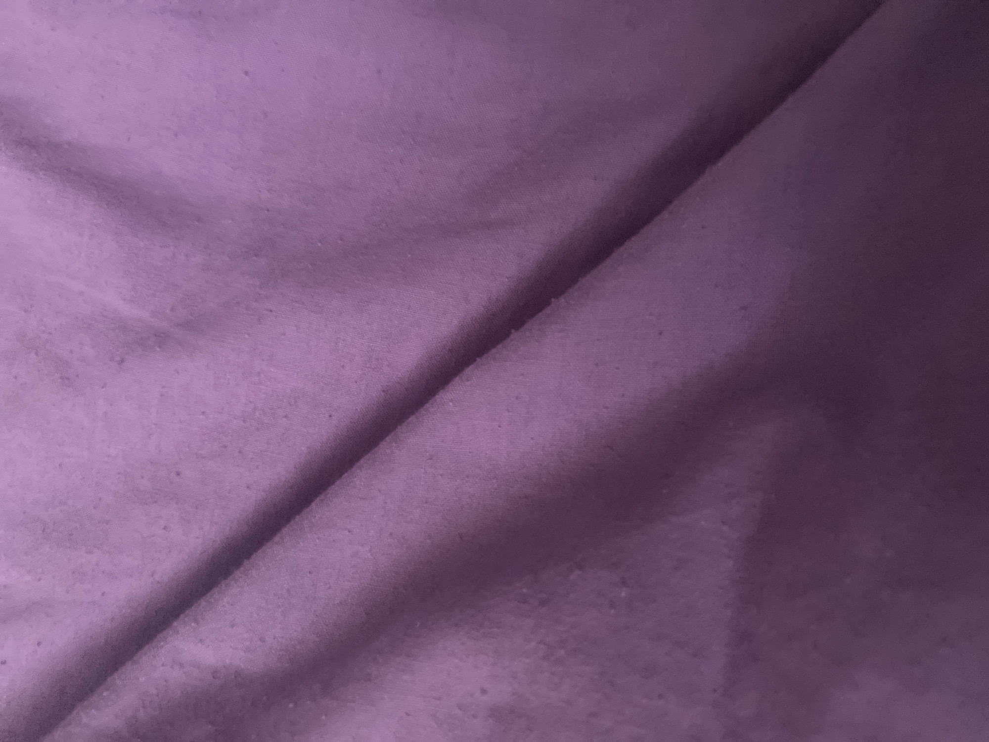 The image shows a close-up, abstract view of a crumpled purple fabric. There are no discernible landmarks or contextual elements to identify a specific location in Kharkiv, Ukraine. The fabric appears to be a textile, possibly clothing or bedding, with slight imperfections or pilling visible in certain areas. The lighting is soft, creating subtle shadows that highlight the folds and textures of the material. The image is solely focused on the fabric itself, with no people, objects, or actions present.