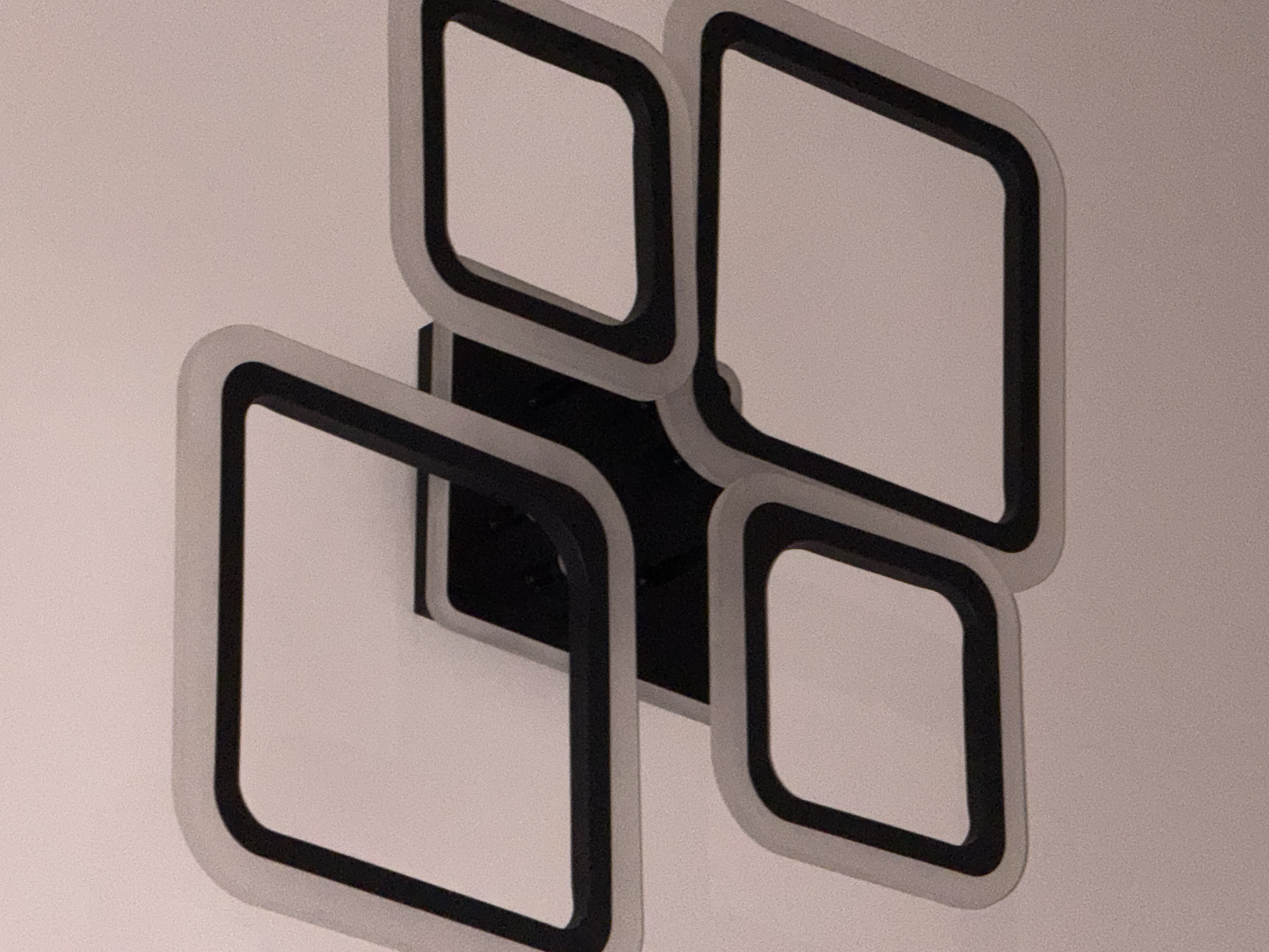 The image is an abstract close-up of a modern ceiling light fixture with multiple interlocking diamond-shaped elements. These elements are outlined in black with a lighter, possibly translucent border. They are arranged in a staggered pattern, suggesting a contemporary design. The background is a plain, light-colored surface, likely a ceiling. The lighting is even, with no harsh shadows. There is no indication of a specific location in Saratov, Russia, as the image focuses solely on the object itself. No people, actions, or interactions are depicted.