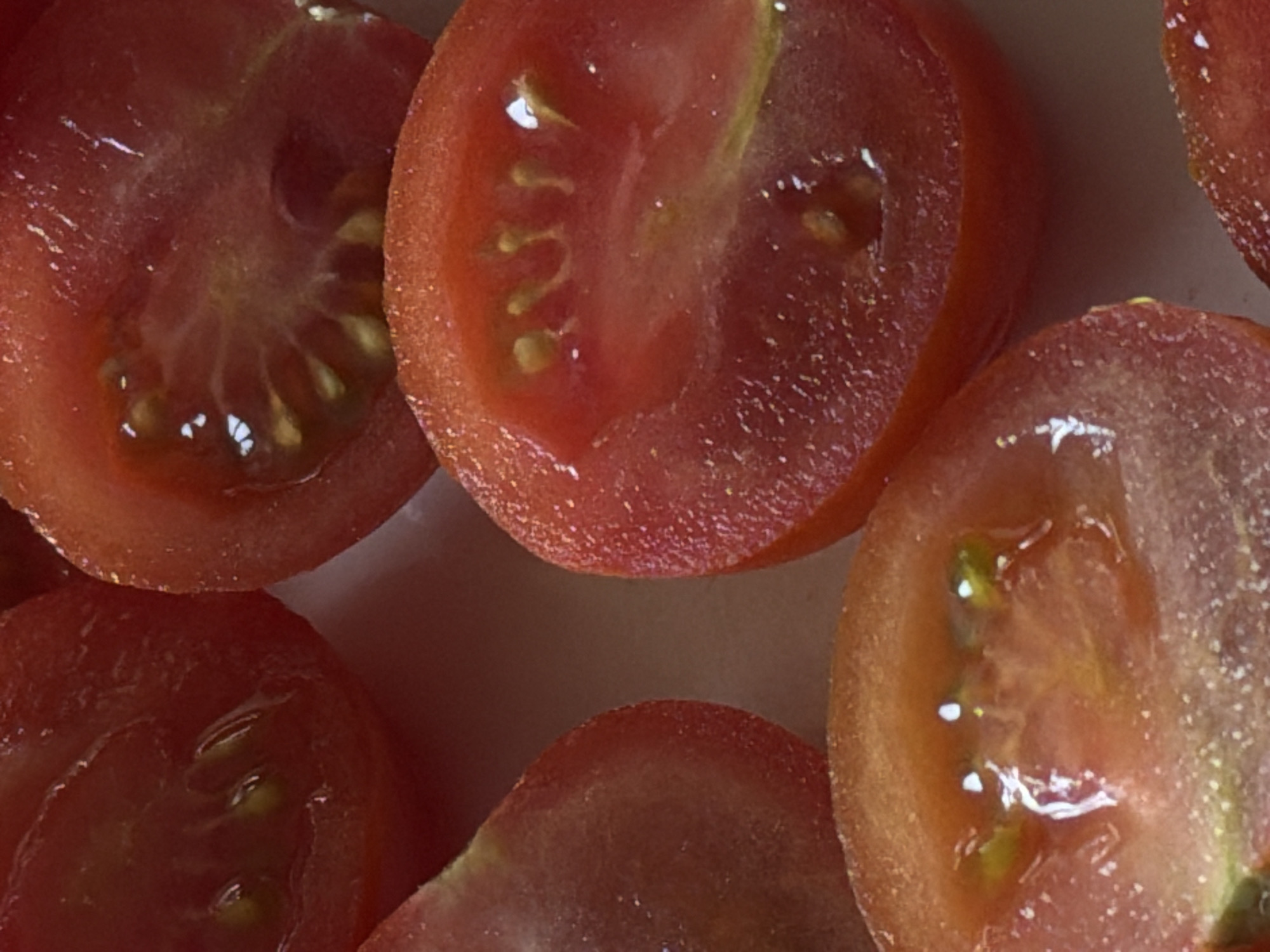 The image shows a close-up of several sliced cherry tomatoes. The slices reveal the inner structure, including the seeds and the fleshy pulp. The tomatoes are various shades of red. There is no indication of the location being Yerevan, Armenia, or any people or actions in the image.