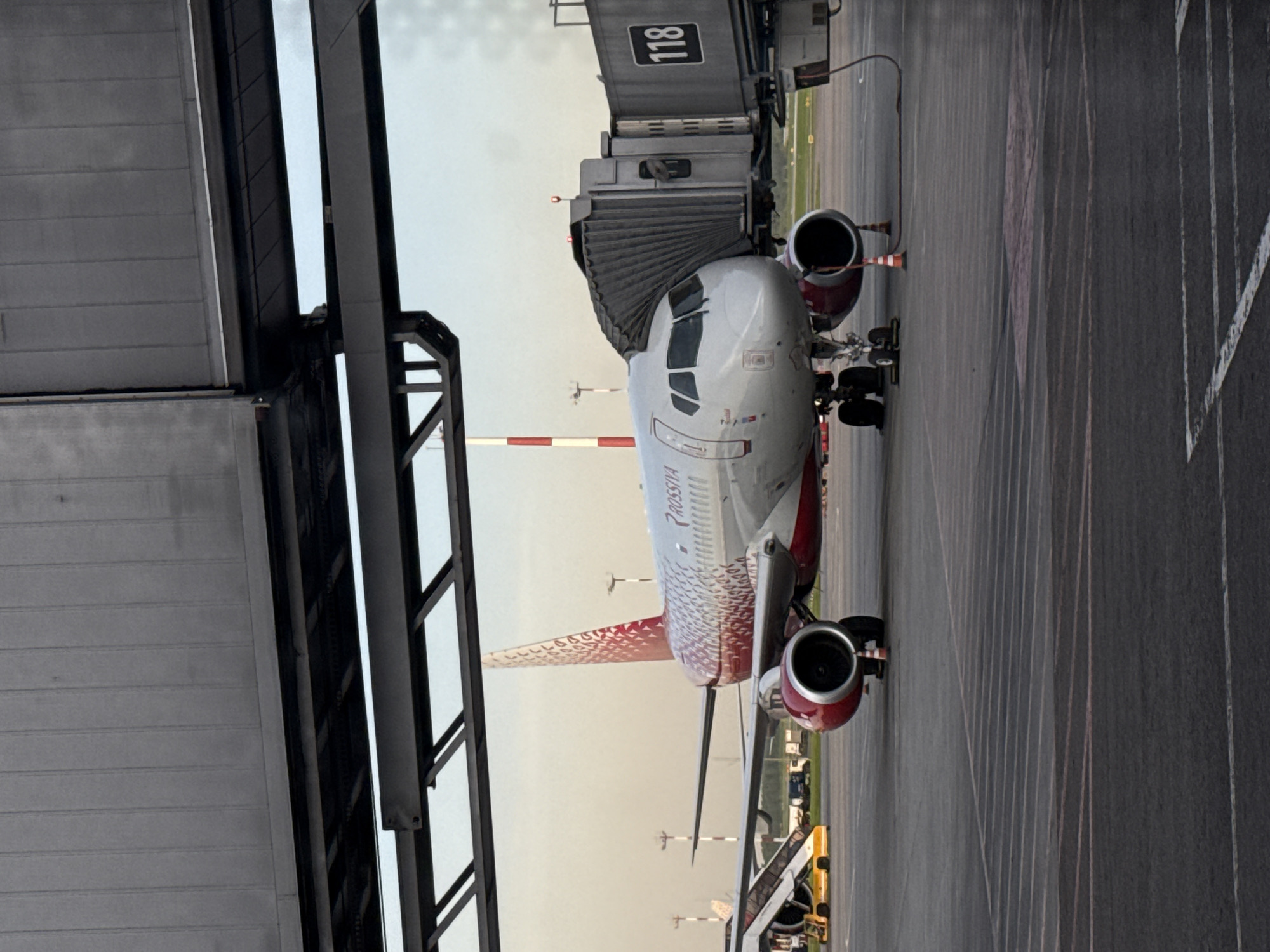 An airplane marked "ROSSIYA" is connected to gate 118 at an airport. The location is speculated to be in Khimki, Russia. The airplane is parked on the tarmac.