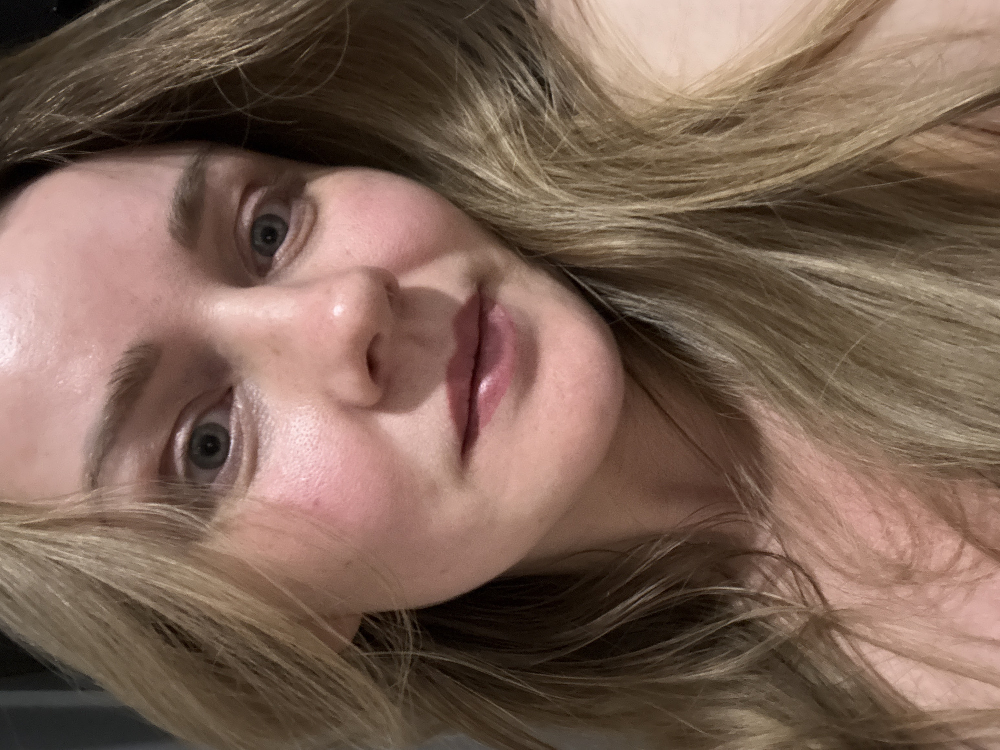 Close-up portrait of a fair-skinned woman with blonde hair. Her eyes are a light color, and her lips are full. The background is blurry. Location is unknown.