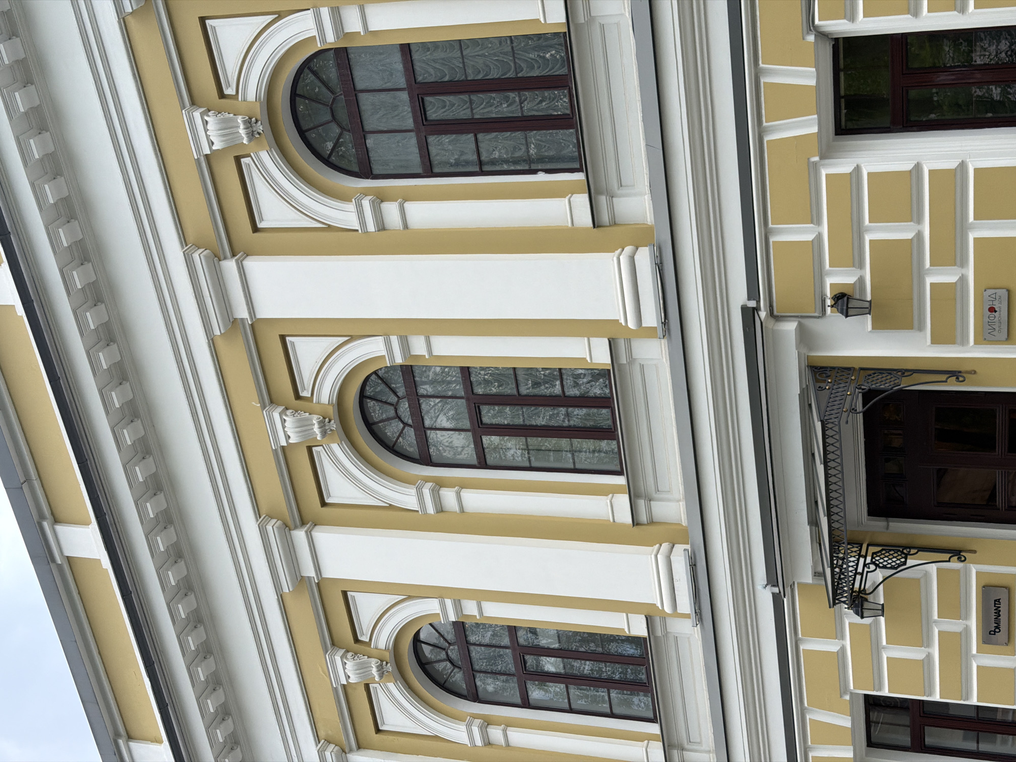 The image shows a building facade in Moscow, Russia. The building has a classical architectural style with arched windows, decorative molding, and a yellow and white color scheme. There are signs in Russian on the building.