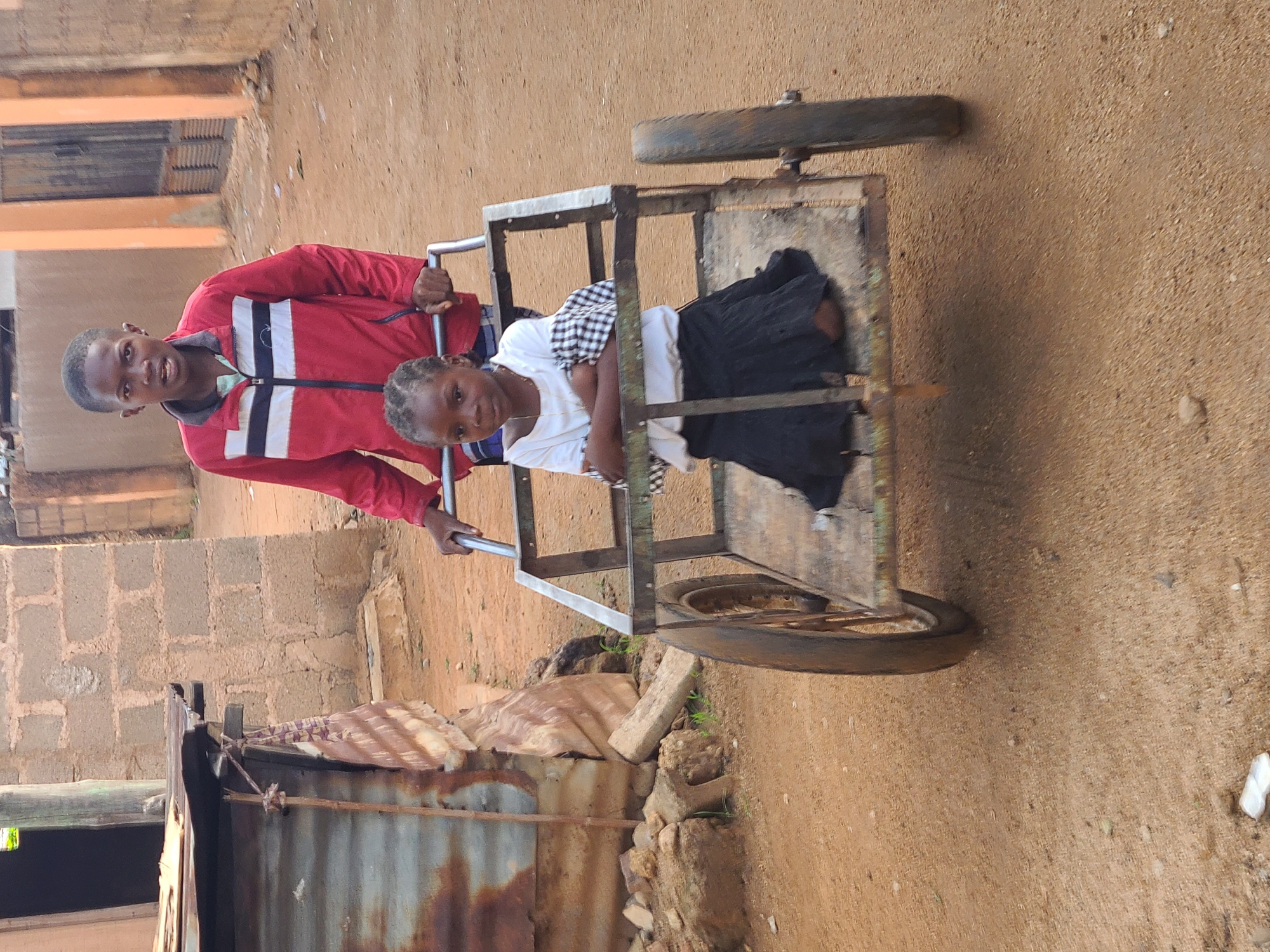 Two children are depicted in an outdoor setting. A young boy, clad in a red jacket with white stripes, stands and pushes a metal cart. Within the cart sits a younger girl, who is wearing a white top and a black and white checkered dress. The cart has two wheels and appears to be homemade. The background shows a dirt road and a building made of blocks. There is also a dilapidated structure. This scene is likely in the city of Jos, Nigeria, as specified in the prompt.