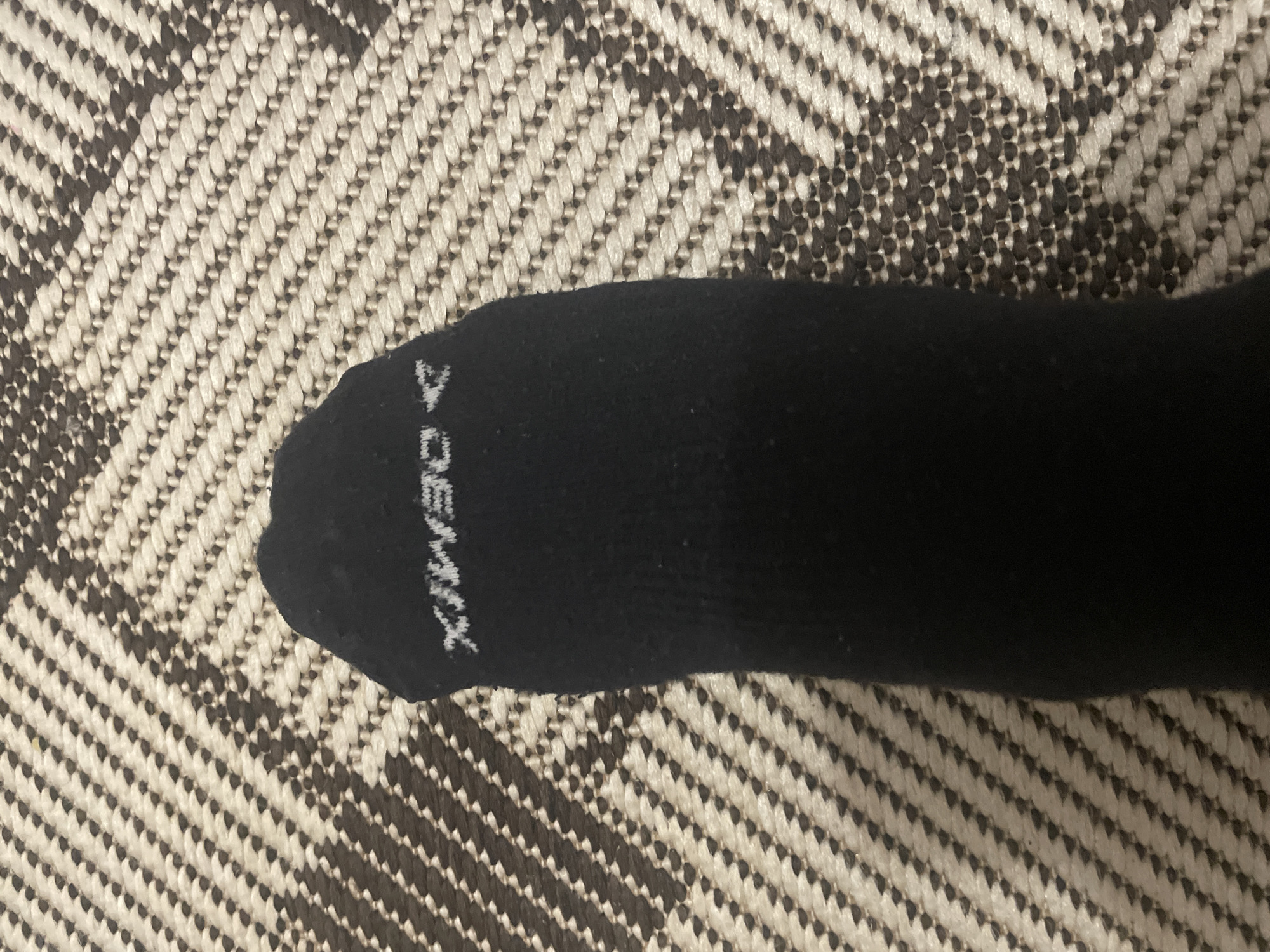 The image shows a black sock with the word "DEMIX" written on it in white. The sock is lying on a rug or carpet with a black and white chevron pattern. The photograph was not necessarily taken in Sarapul, Russia.