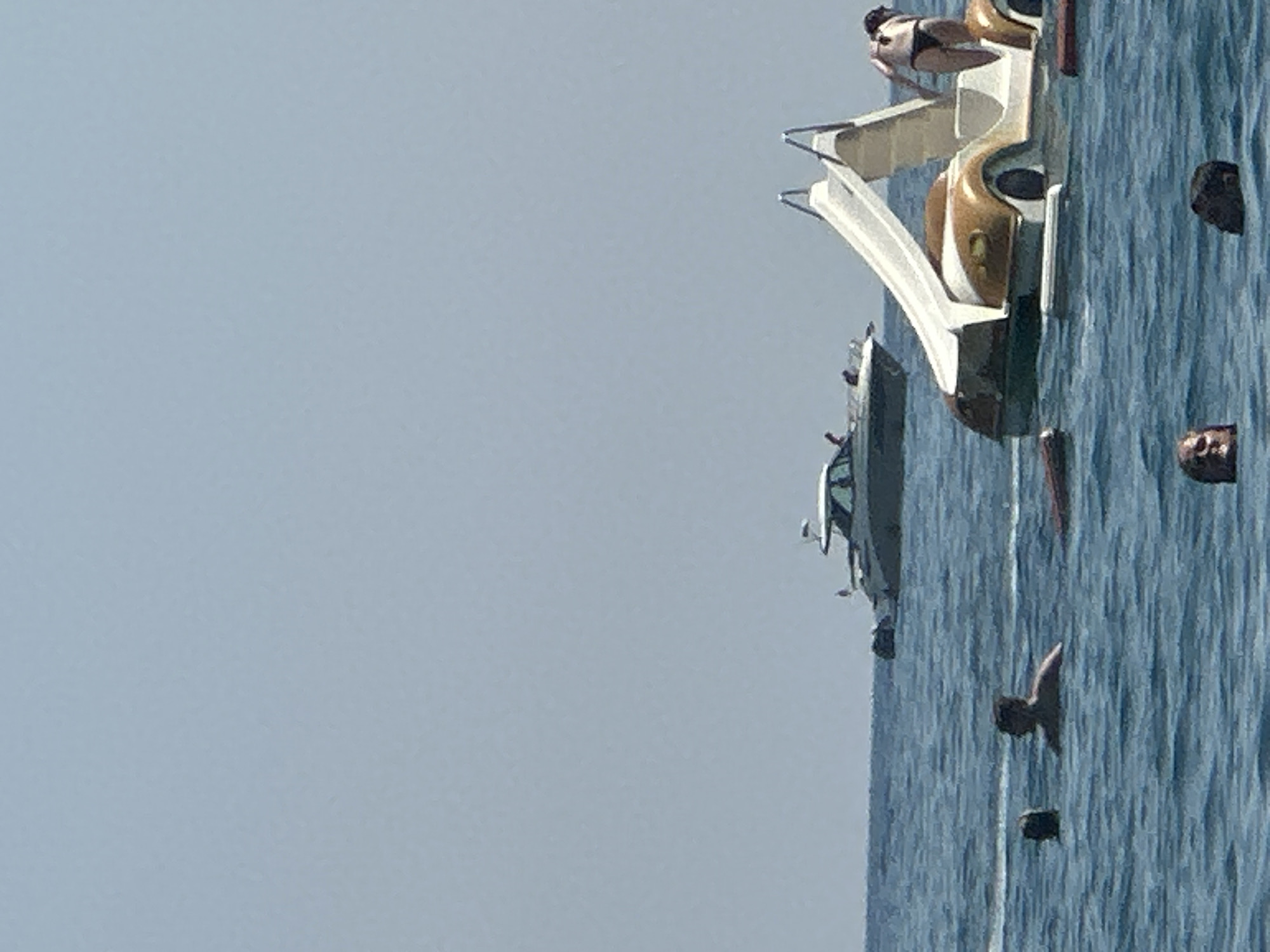 The image depicts a bright, sunny day at a beach in Boreti, Montenegro. The water is calm and blue. In the foreground, several people are swimming in the sea. One person's head is visible above the water, and another is partially submerged. Further out in the water, a boat with a white canopy is cruising. To the right of the boat is a pedal boat designed to look like a car, complete with a slide. A person in a bikini is standing at the top of the slide. Several people are also visible in the water around the pedal boat.