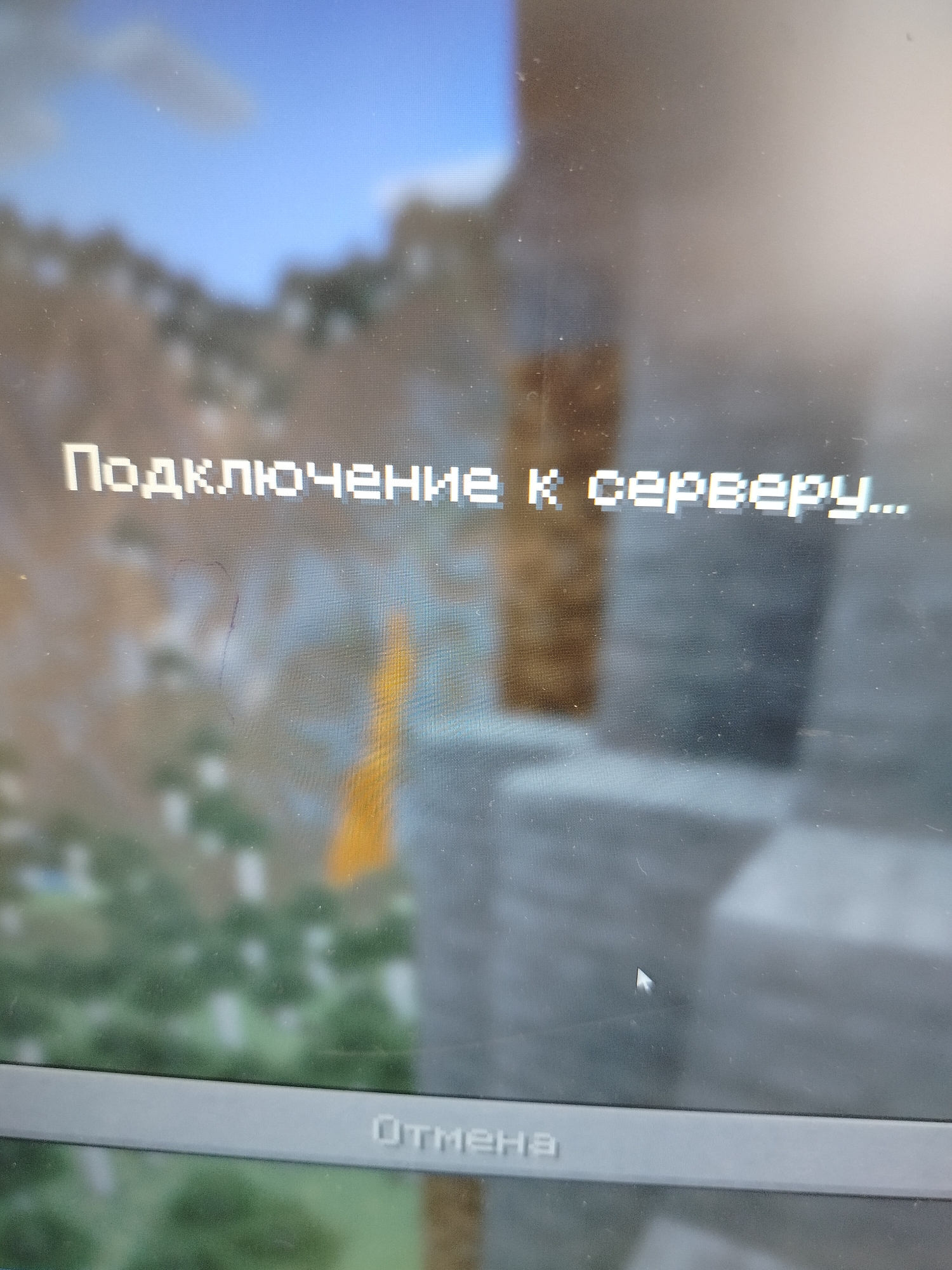 The image shows a computer screen displaying the game Minecraft. The text "Подключение к серверу..." (Connecting to the server...) is visible, along with the button "Отмена" (Cancel). The in-game environment visible is a blurred landscape with mountainous terrain and structures. A mouse cursor is also visible on the screen. The location is not discernible from the information in the image. It is impossible to give a location.