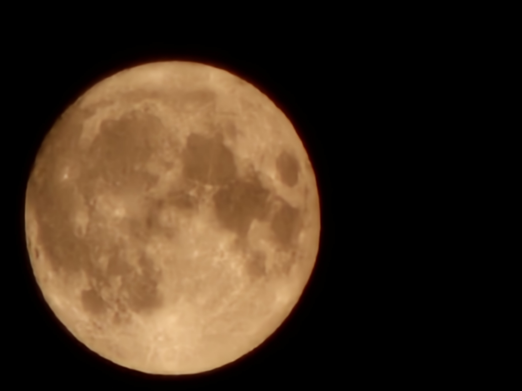 The image shows a full moon in a dark sky. The moon appears orange-yellow and takes up most of the left side of the frame. The right side is black. There is no information in the image to suggest that the image was taken in Denpasar, Indonesia.