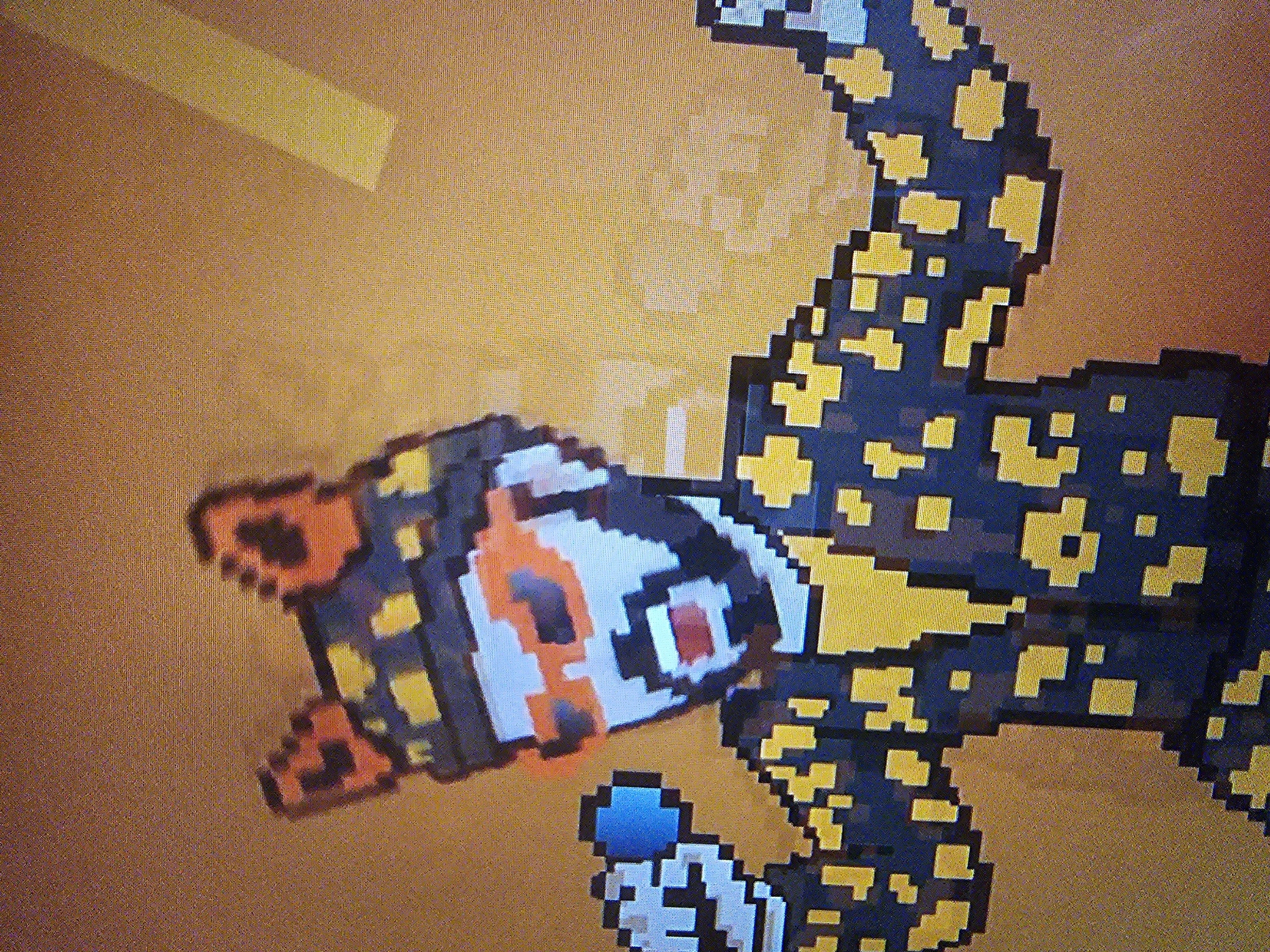 The image depicts a pixelated, digital rendering of a stylized tiger-like creature with a black body and yellow spots. The head is white with orange markings around the eyes and nose. The tail is curved upward. The background is a solid orange color with a yellowish horizontal bar in the top left corner. There is no indication of Holywell, United Kingdom in the image.