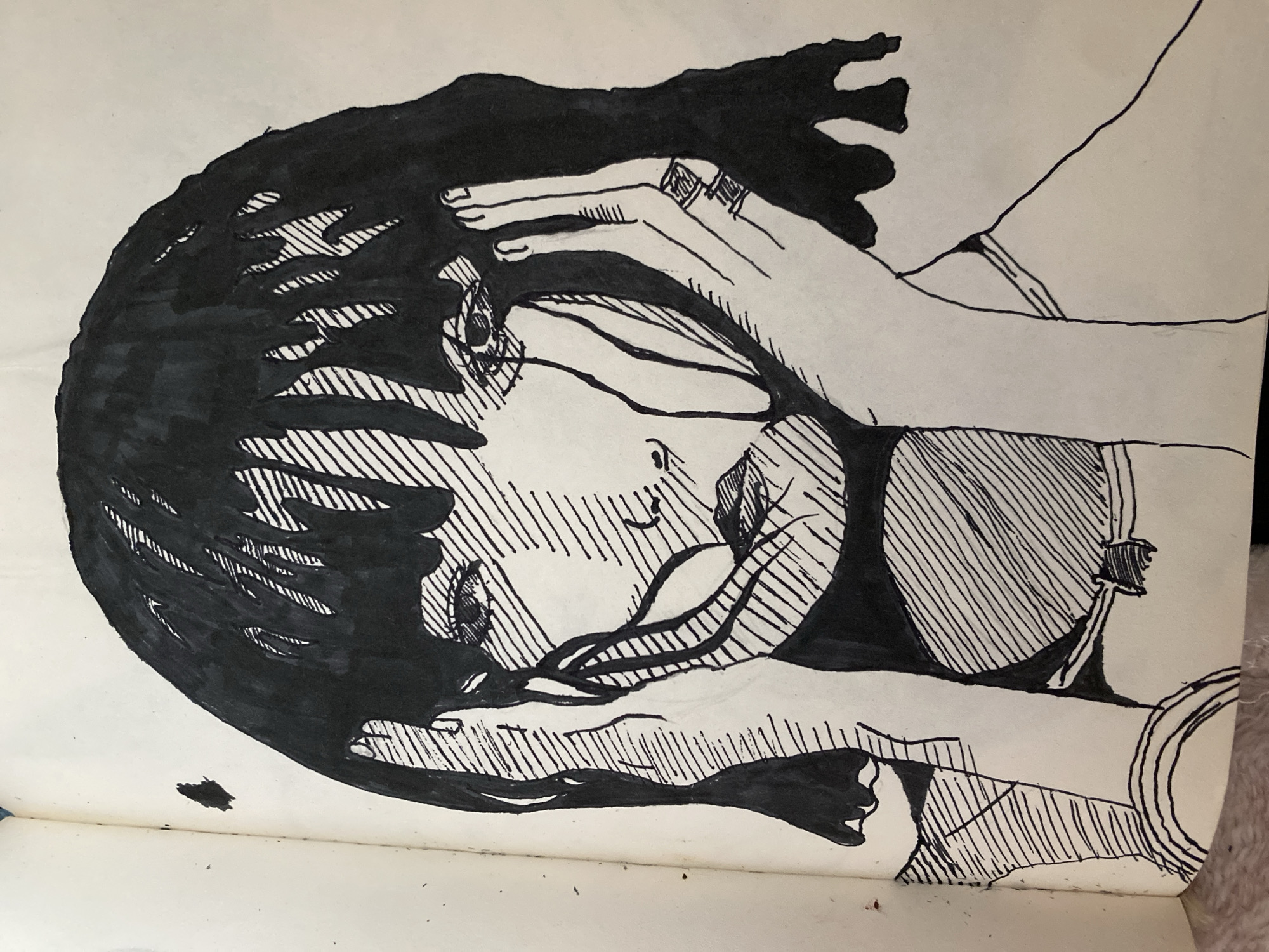 This is a black and white ink drawing on paper, likely from a sketchbook, depicting a person in a somewhat abstract style. The main subject appears to be a face, possibly of a young woman, shown in profile and tilted downwards. Dark, scribbled lines form the hair, which is voluminous and obscures parts of the face. Two hands are prominently featured, one reaching over the head and touching the forehead, and another appearing to support the chin or jawline from below. These hands are drawn with thin lines, and one has rings on its fingers.
The drawing utilizes a technique of cross-hatching to create shading and depth, particularly on the face, neck, and torso area. The expression on the face is difficult to discern with certainty due to the stylistic rendering, but there are subtle indications of closed eyes and perhaps a hint of emotion, possibly sadness or contemplation, suggested by the slight downturn of the mouth and the shading around the eyes. The body is partially visible, with lines suggesting clothing, possibly a top with straps or a neckline.
The overall mood of the artwork is intimate and possibly melancholic, focusing on the portrait of the individual and the interaction with their own hands. The background is largely blank white paper, with some smudges and a small ink splotch at the bottom left. There is no visible text in the image. The setting is unspecified by the artwork itself, though external information places it in Zhmerynka, Ukraine. The time of day and weather are not indicated.