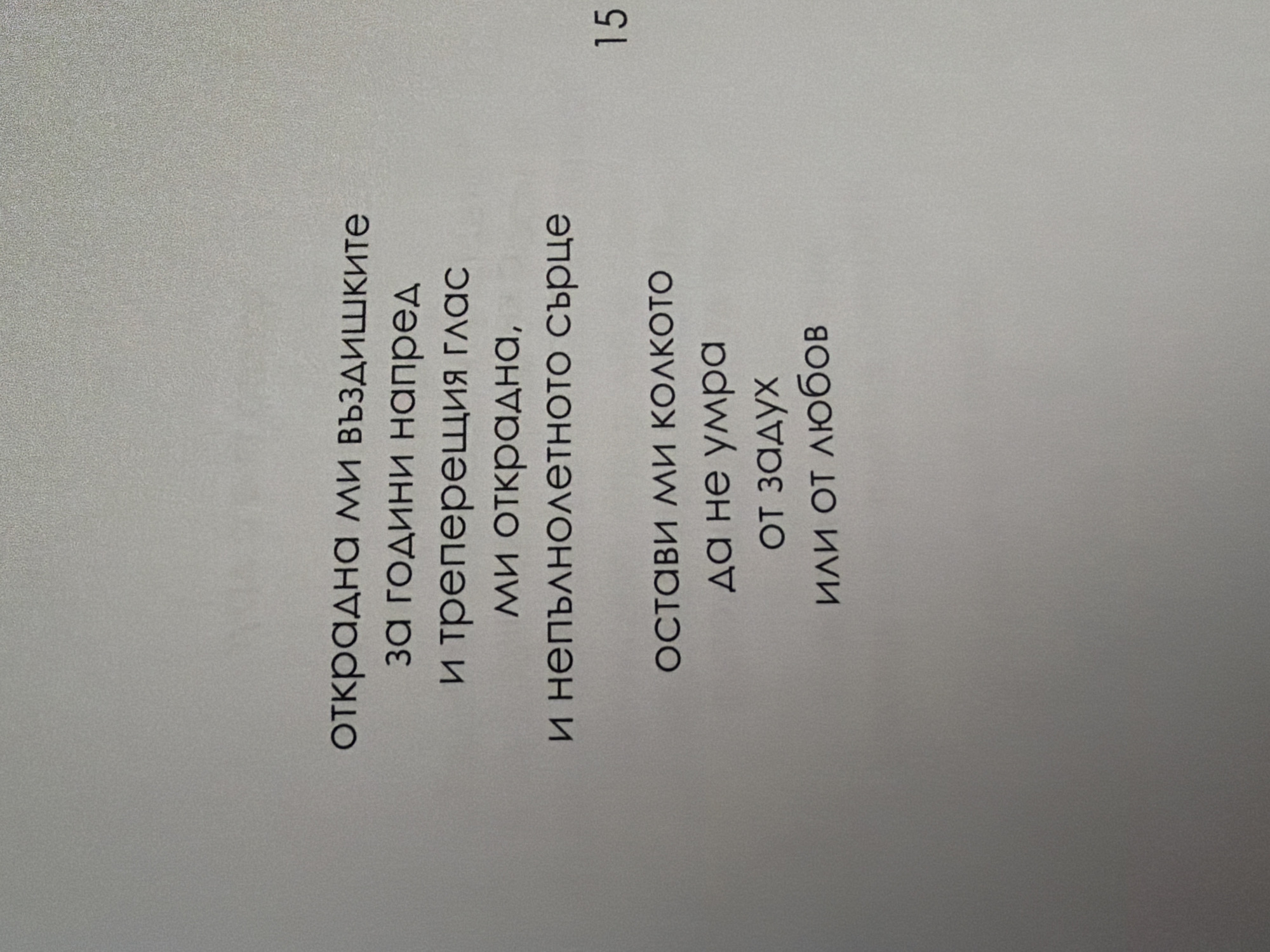 The image displays a page from a book with text in Bulgarian. The text appears to be a poem. The page also has a page number "15" in the lower right corner. The background is a textured light gray. There are no people, actions, or interactions visible in the image. The environment is an indoor setting, likely a book or document. There is no information in the image to connect it to the city of Pazardzhik, Bulgaria.