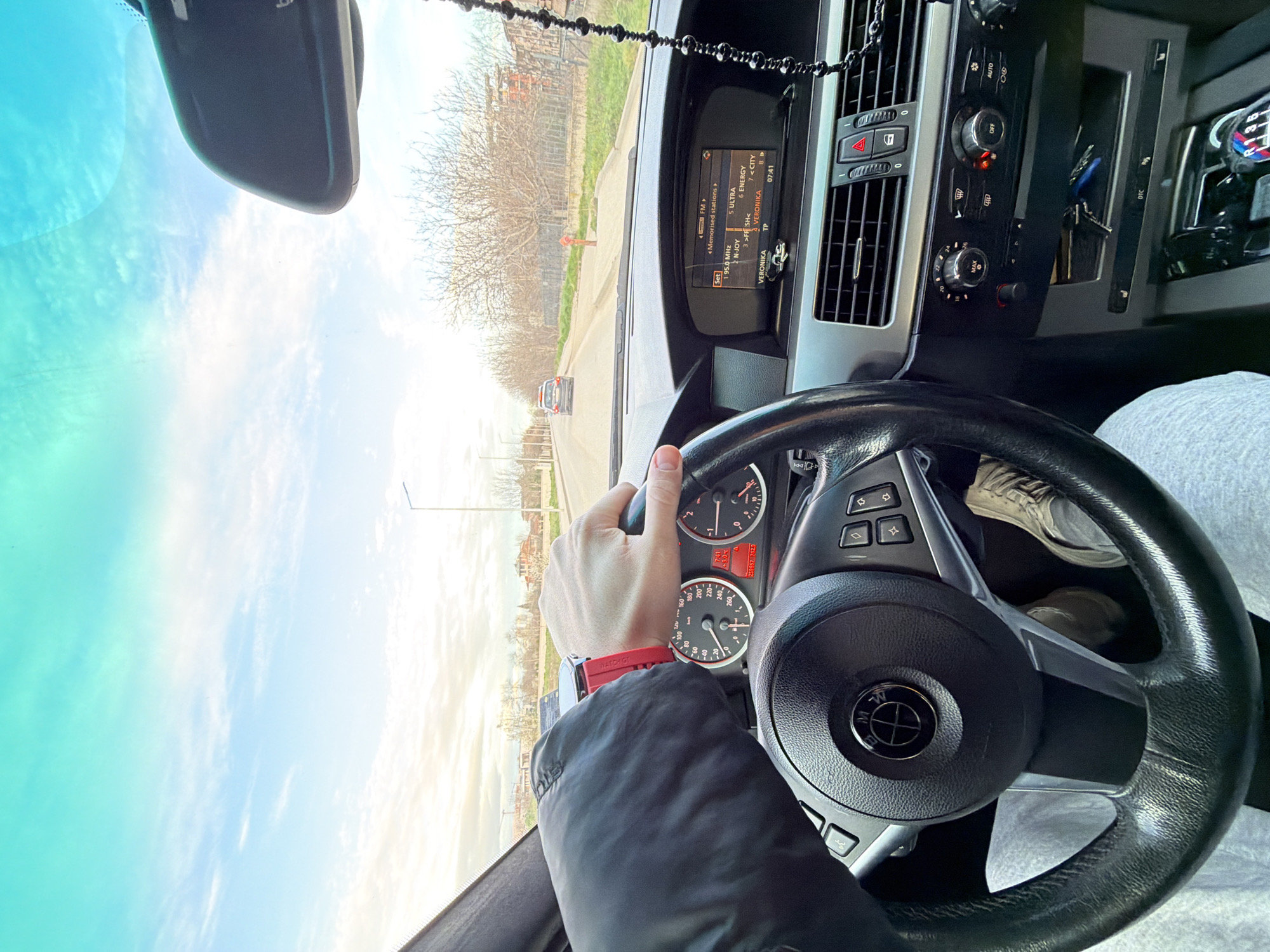 The image is taken from inside a car, likely in Plovdiv, Bulgaria based on the radio station "VERONIKA" displayed on the car's infotainment system. The driver is holding the steering wheel, with a red watch visible on their left wrist. The car is moving on a road with buildings and trees on either side. A red fire hydrant is visible on the right side of the road in the distance. The car's dashboard displays the time as 07:41 and the mileage as 259557 742.3. The car's radio is tuned to 95.0 MHz.
